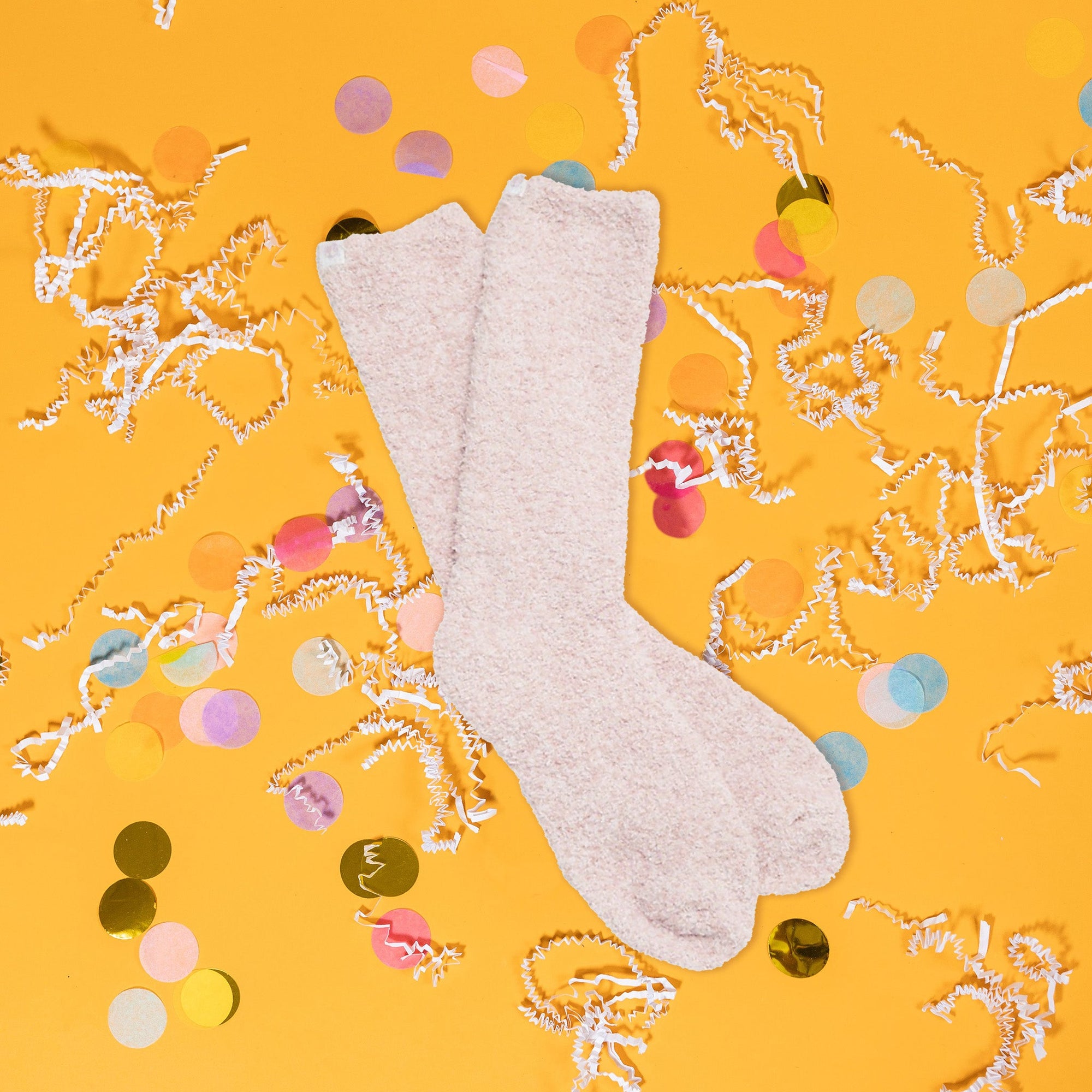 On a sunny mustard background sits a pair of socks with white crinkle and big, colorful confetti scattered around. These heathered socks are dusty rose and white and so soft.