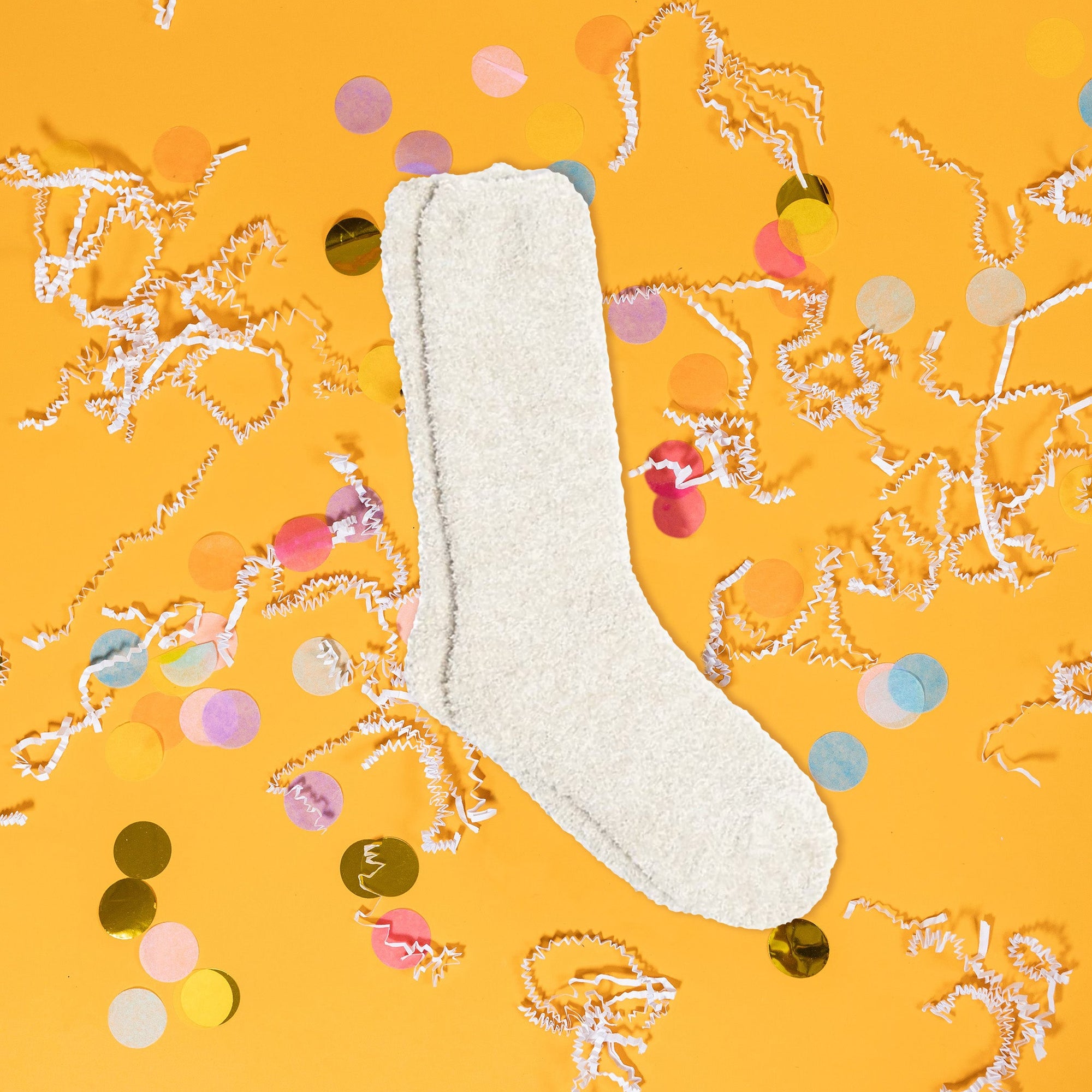 On a sunny mustard background sits a pair of socks with white crinkle and big, colorful confetti scattered around. These heathered socks are stone and white and so soft.
