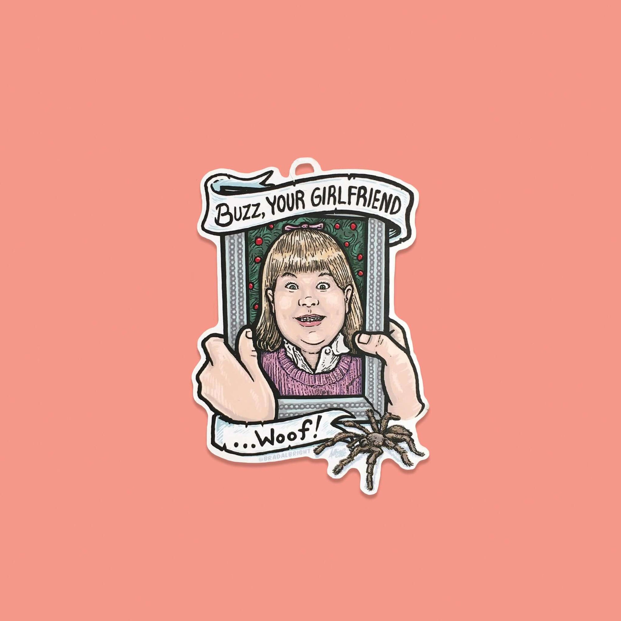On a coral pink background sits a Home Alone inspired wood ornament. It is a picture frame of Buzz's girlfriend and it says "BUZZ, YOUR GIRLFRIEND... WOOF!" on white banners, in black lettering. There is a tarantula at the bottom