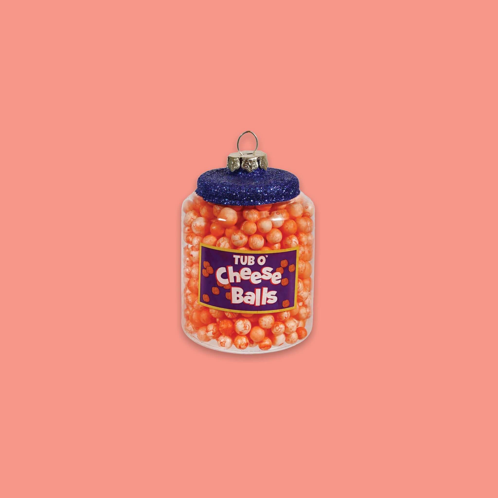 On a geometric light and medium pink background sits a container of cheese balls ornament. This 'TUB O' Cheese Balls' glass ornament is filled with cheese balls. It has a navy glitter lid.