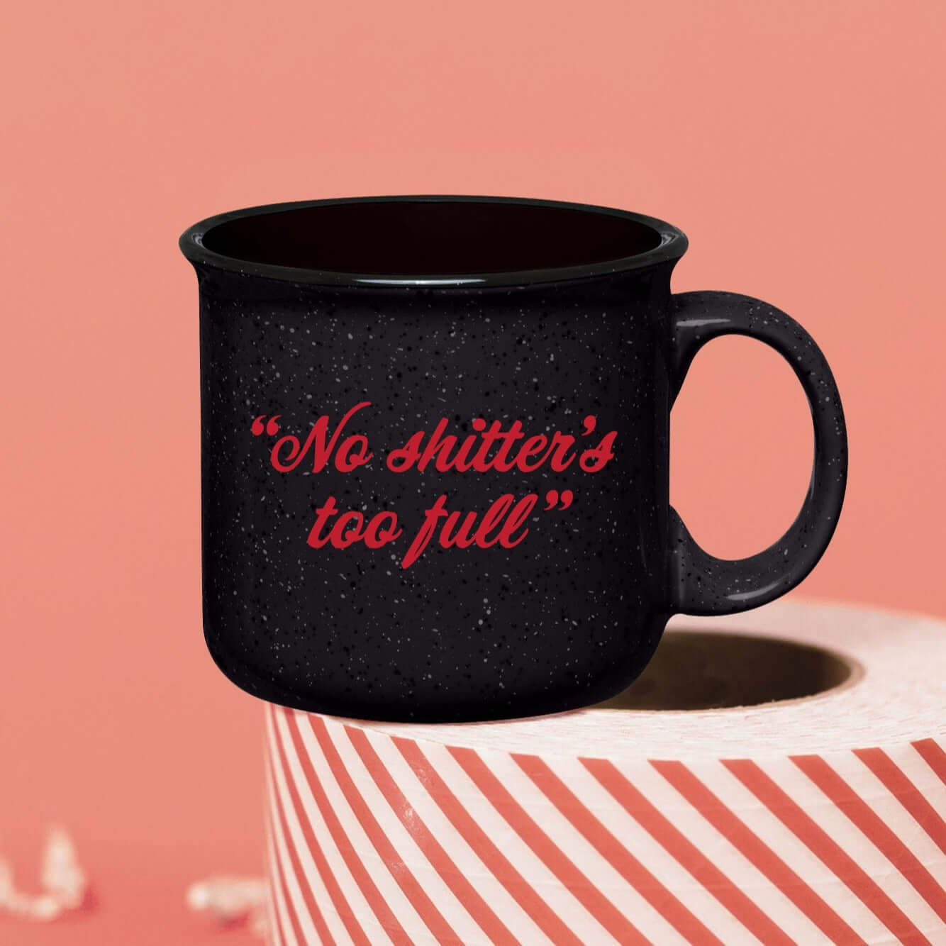 On a pink coral background sits a campfire mug on a roll of red and white packing tape. There is white crinkle. This Christmas Vacation inspired mug is charcoal grey with black and white specks and it's say in red lettering "No shitter's too full."