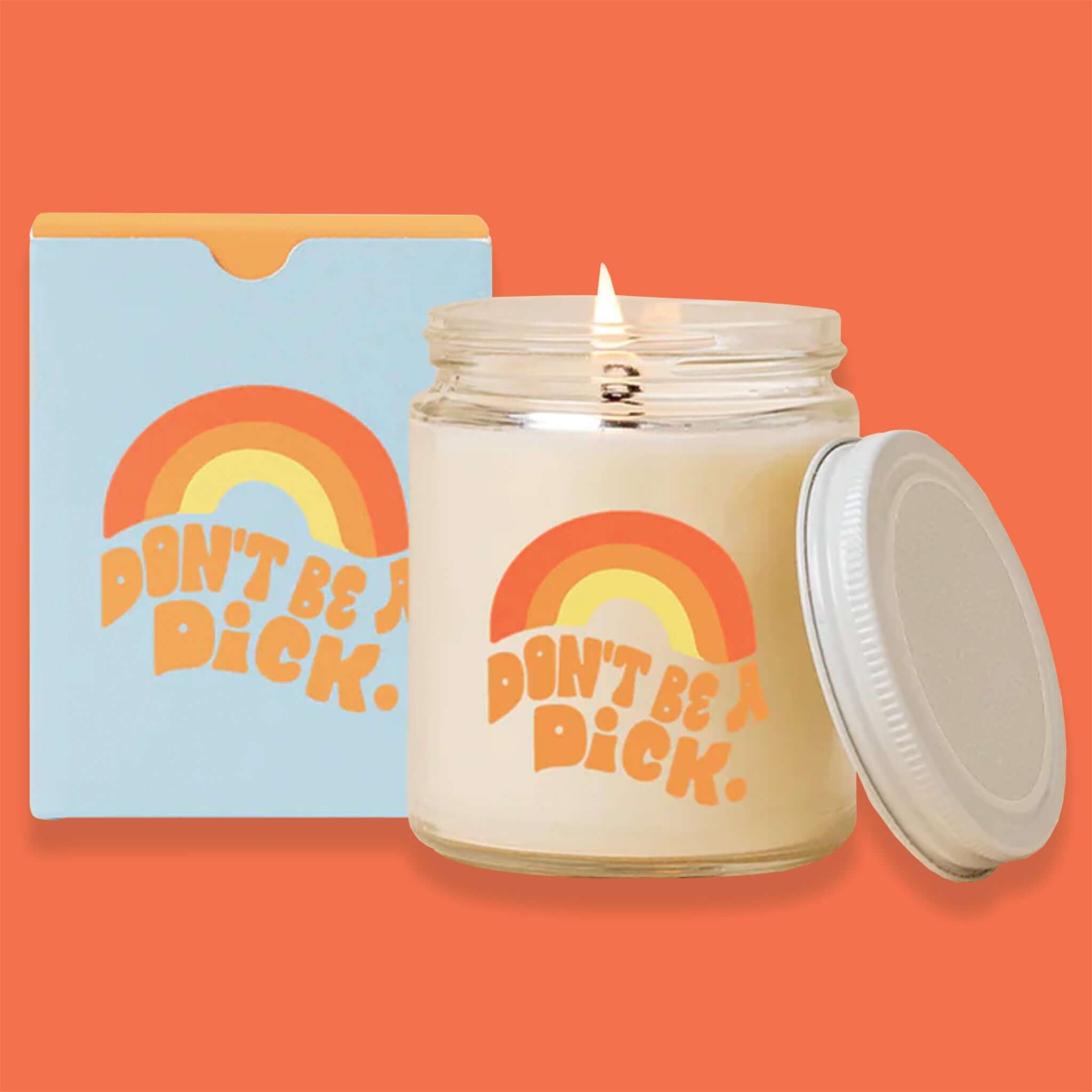 On an orangey-red background sits a box and a candle. The box is a package for the candle. It is light blue with a rainbow graphic on the front in orange, mustard orange and yellow. Under it says "DON'T BE A DiCK." in a groovy, orange handwritten font. Next to it is a glass candle that is lit, with the same rainbow graphic and saying and there is a white lid leaning against it.
