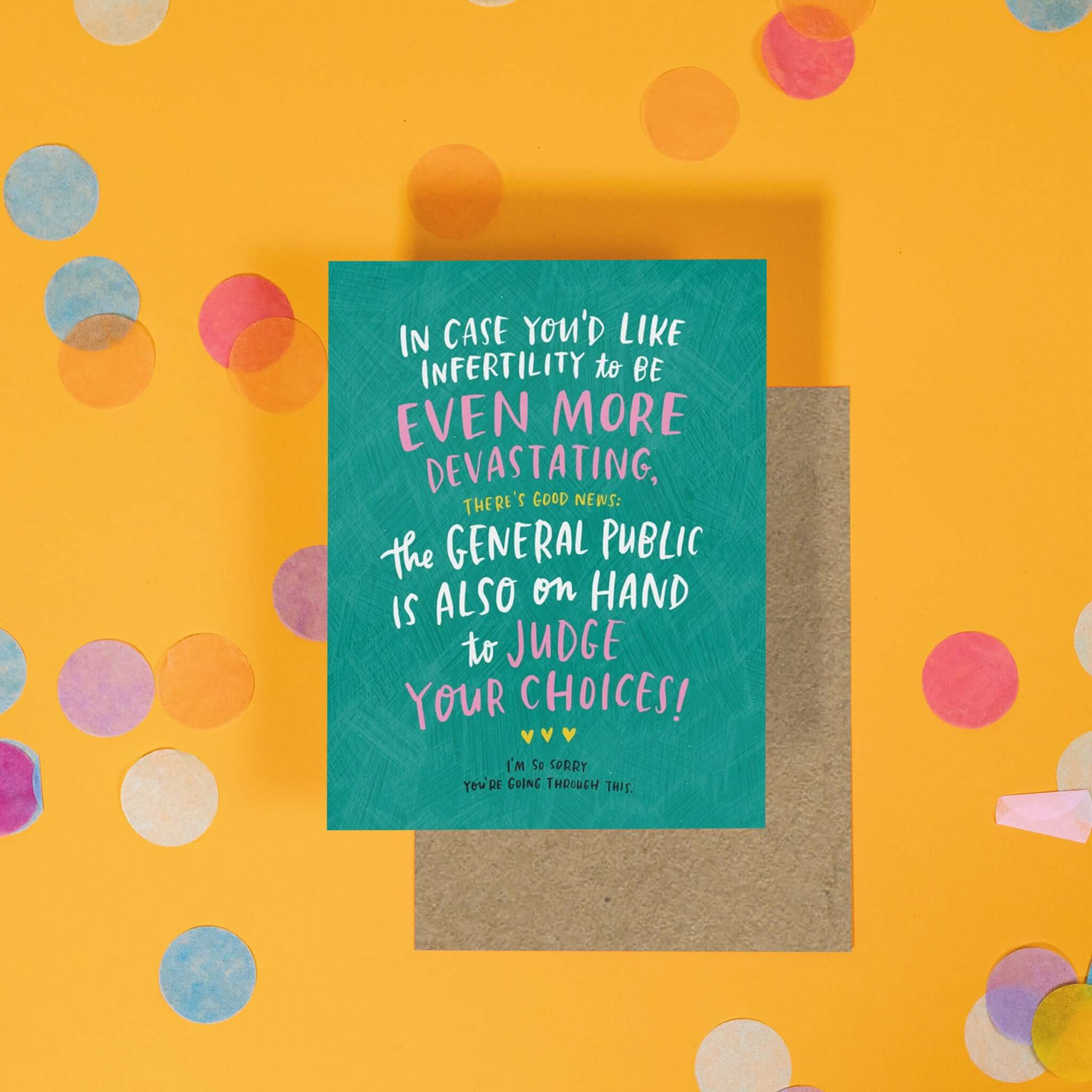 On a sunny mustard background is a greeting card and envelope with big, colorful confetti scattered around. The teal greeting card says "In case you'd like infertility to be even more devastating, there's good news: the general public is also on hand to judge your choices!" in white, pink, and yellow handwritten lettering. Under that are three yellow hearts and it says "I'm so sorry you're going through this." in black handwritten lettering. A kraft envelope sits under the card.