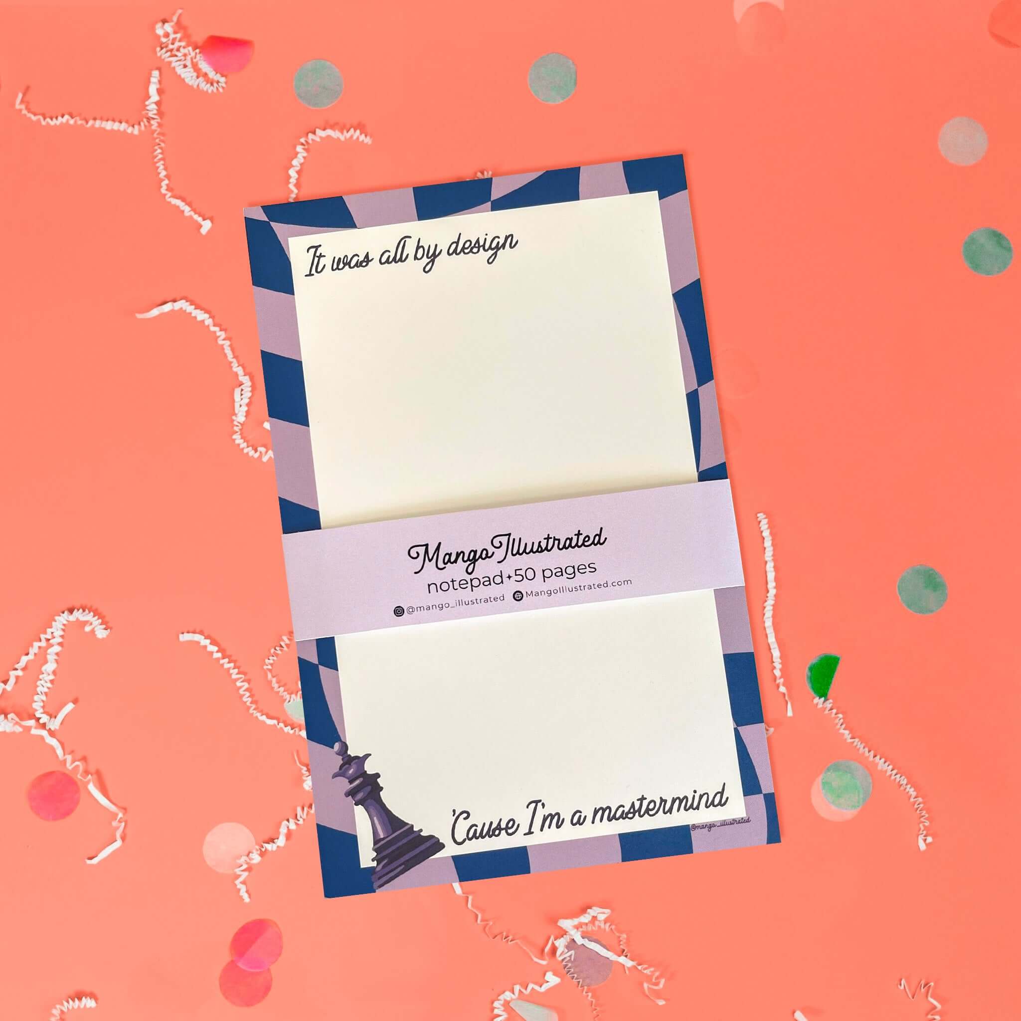 On a coral pink background sits a notepad with white crinkle and big, colorful confetti scattered around. This Taylor Swift inspired notepad is in navy and lavender with a cream background and it says at the top "It was all by design" in black script lettering and at the bottom it says "'Cause I'm a mastermind" in black script lettering. There is a chess piece illustration.