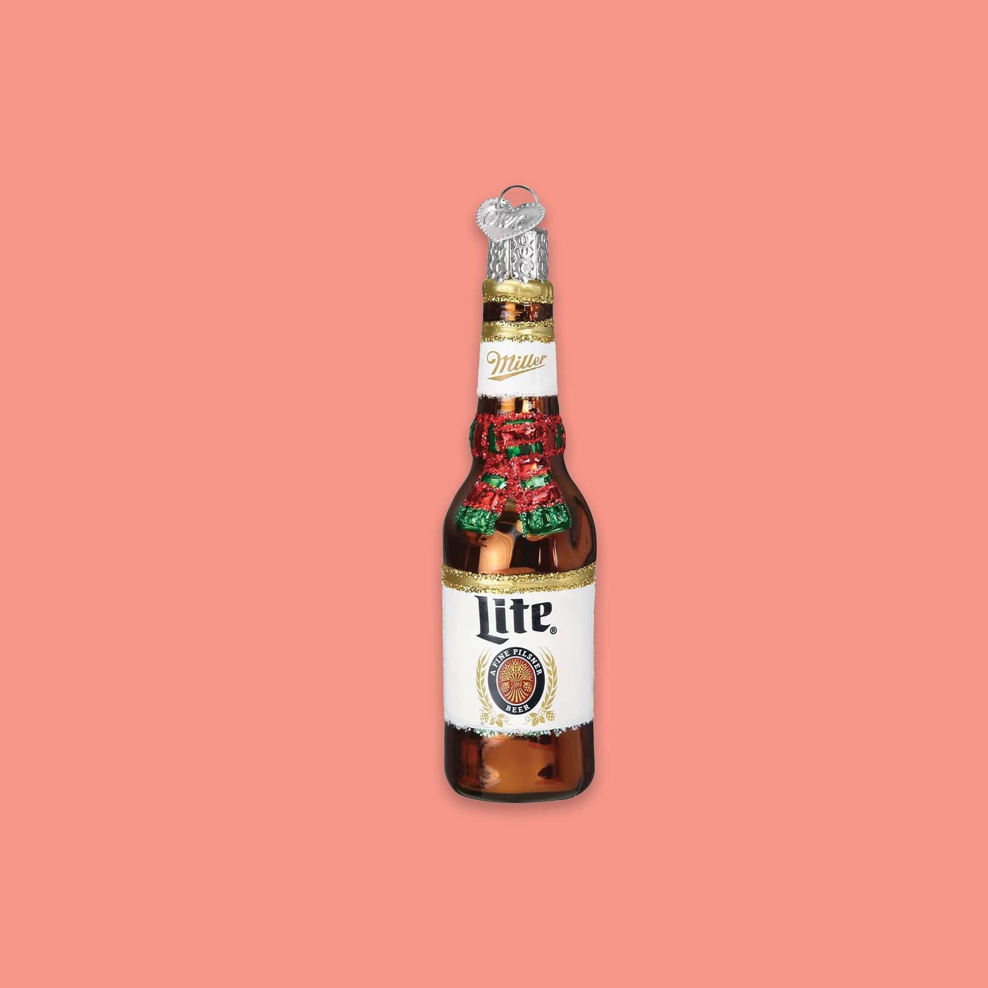 On a coral pink background sits a bottle ornament. This is a glass Miller 'Lite' holiday bottle ornament. It has a red and green glitter scarf around the neck of the bottle.