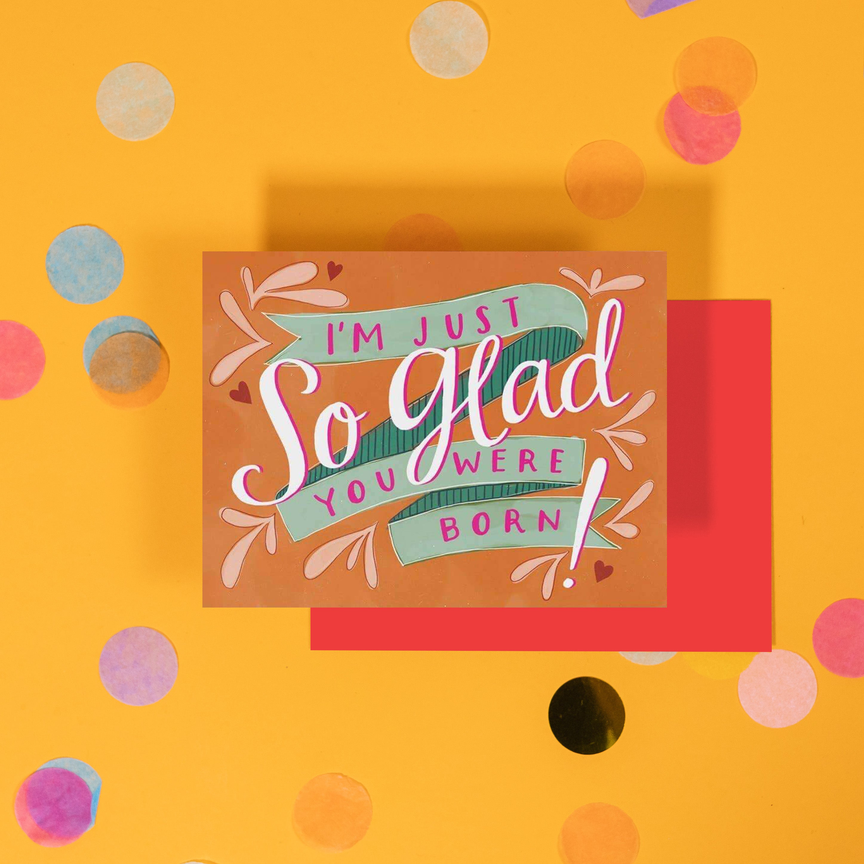 On a bright yellow background with colorful confetti sits a birthday card that reads "I'm Just So Glad You Were Born!" in white script and pink print with a light green ribbon banner.