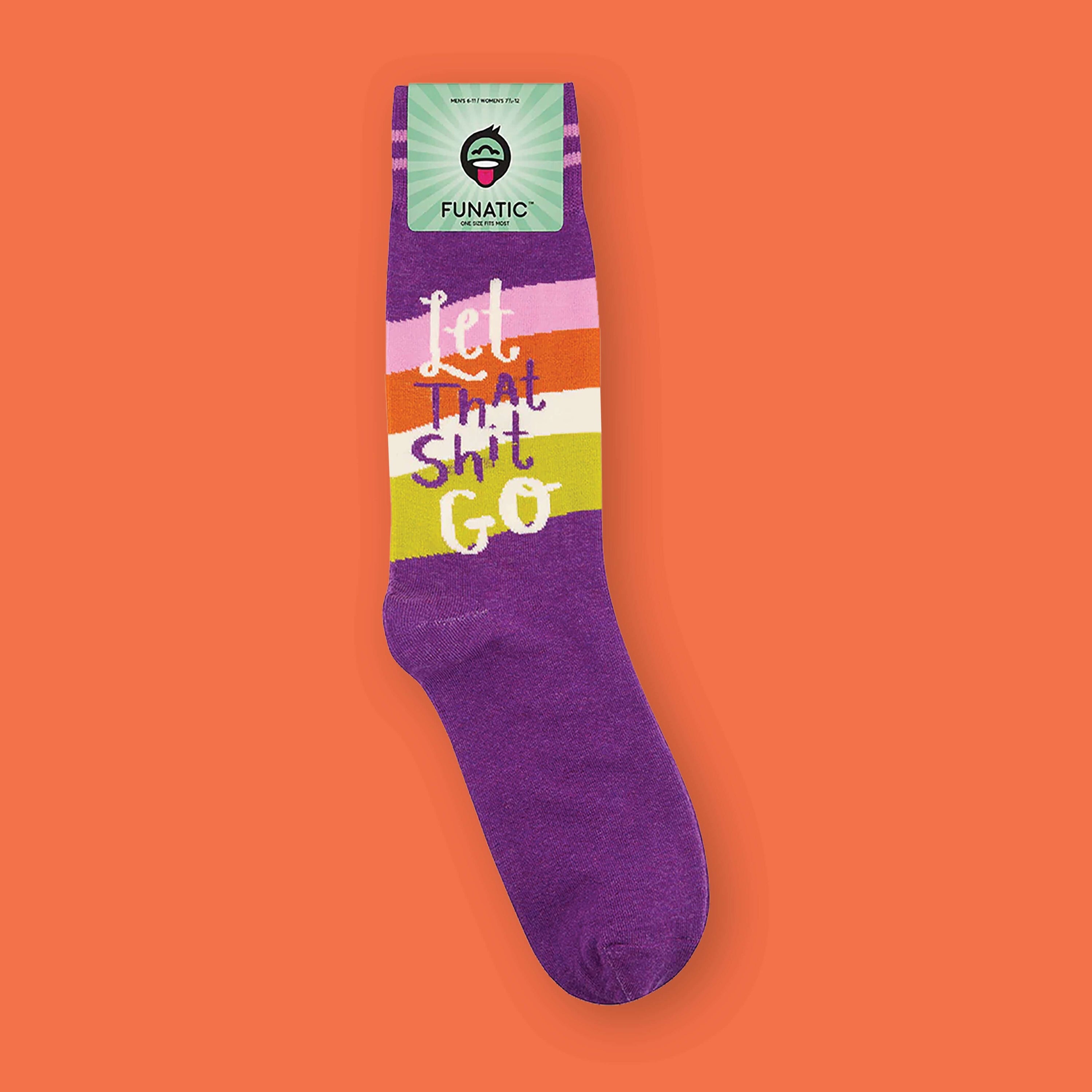 On an orangey-red background sits a sock. This purple sock has pink stripes at the top and various colored stripes in the middle. They are pink, orangey-red, white, and chartreuse. It says in white and purple "Let That Shit Go" in handwritten lettering.