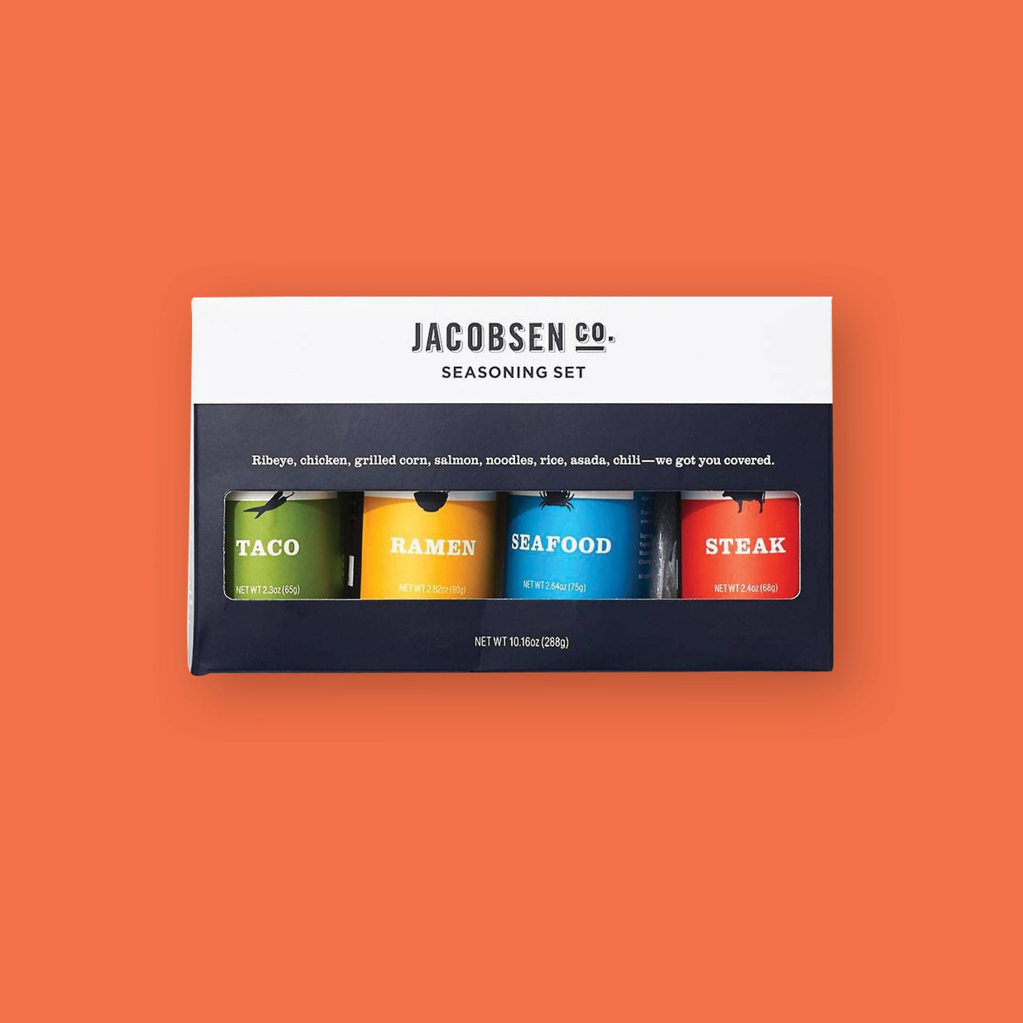 On an orangey-red background sits a box and four jars. The box is black and white with a see-thru window. It says "JACOBSEN CO. SEASON SET" in black, call caps block font. Under it says "Ribeye, chicken, grilled corn, salmon, noodles, rice, asada, chili - we got you covered." in white, sreif font. The bottles are seasons of "Taco" in green label, "Ramen" in yellow label, "Seafood" in blue label, and "Steak" in red label. Each is 2.40z(68g)