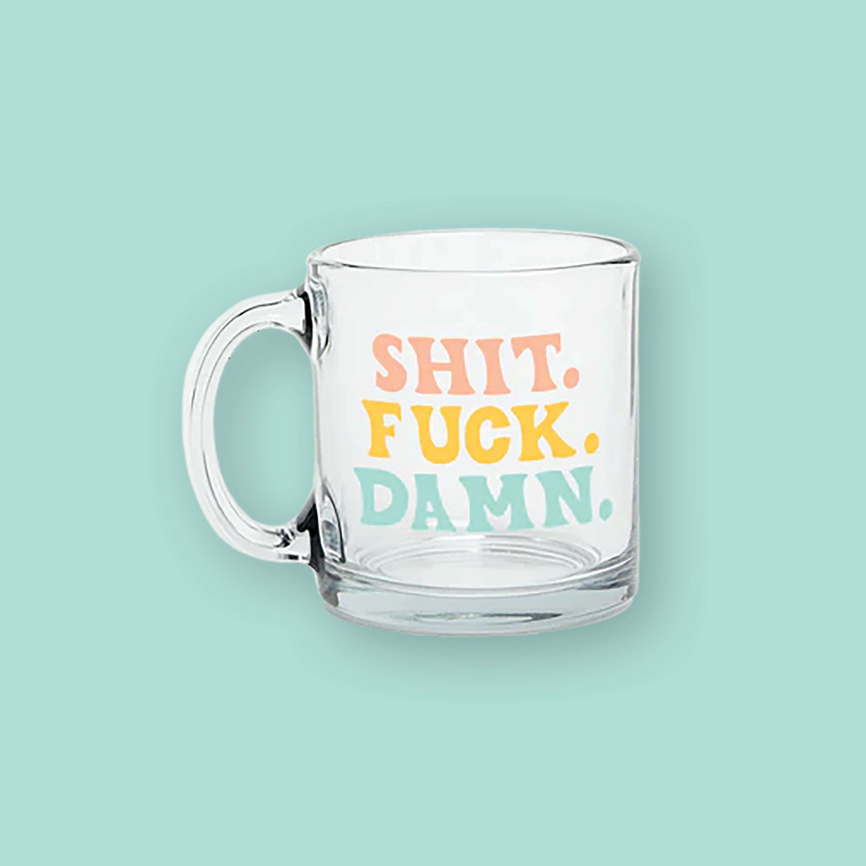 On a mint background sits a mug. This clear mug says "SHIT. FUCK. DAMN." in all caps, bold handwritten lettering. The word "SHIT." is in light coral. The word "FUCK." is in sunny mustard and the word "DAMN." is in mint.