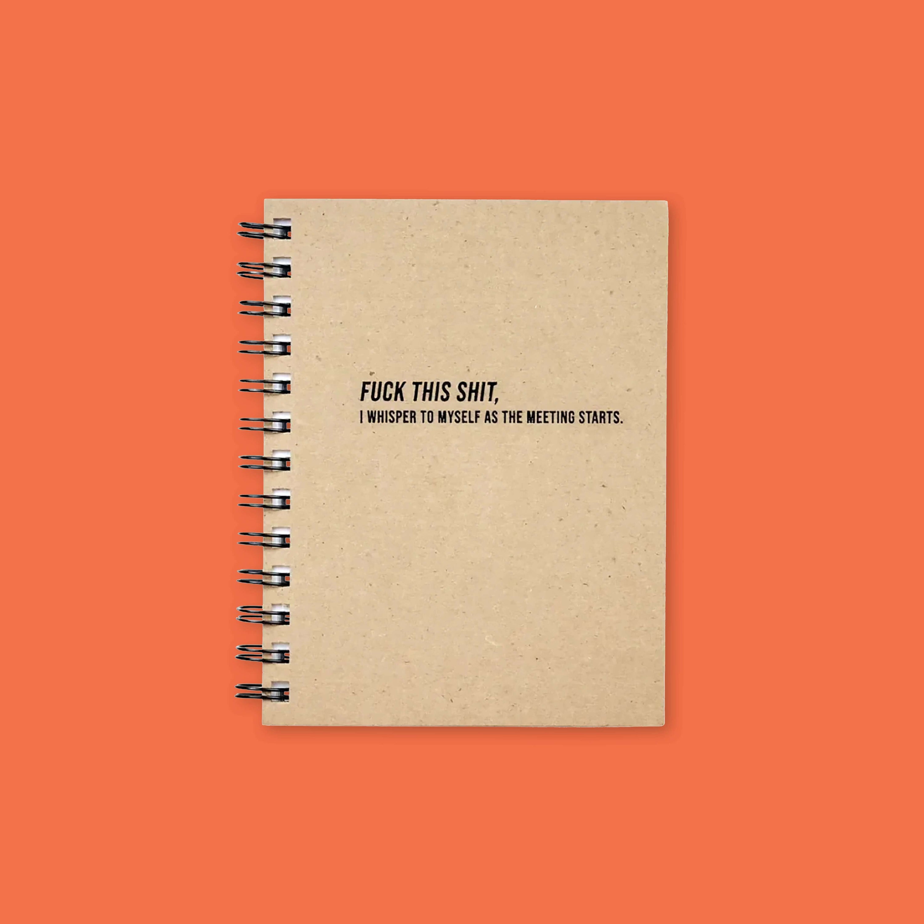 On an orangey-red background sits a kraft hard cover spiral-bound notebook with white striped paper that says "FUCK THIS SHIT (I whisper to myself as the meeting starts)," in black, all caps block font.