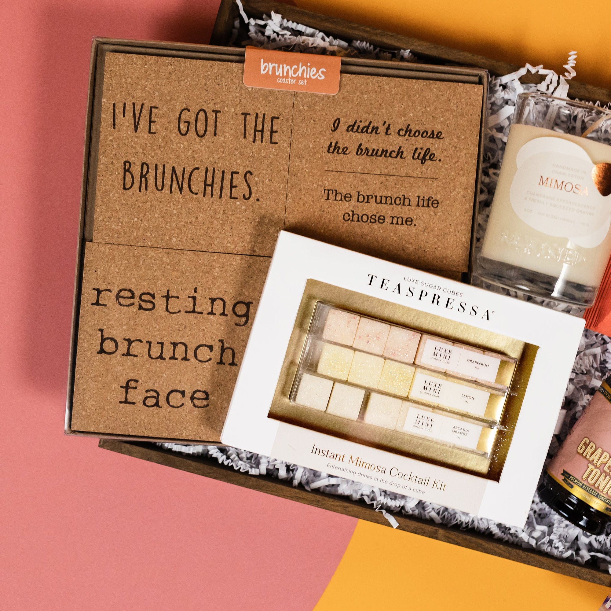 On a funky light orange and coral background sits a wooden tray filled to the brim with brunch accoutrements. This photo is a close-up of our favorite Teaspressa Instant Mimosa Cocktail Kit.