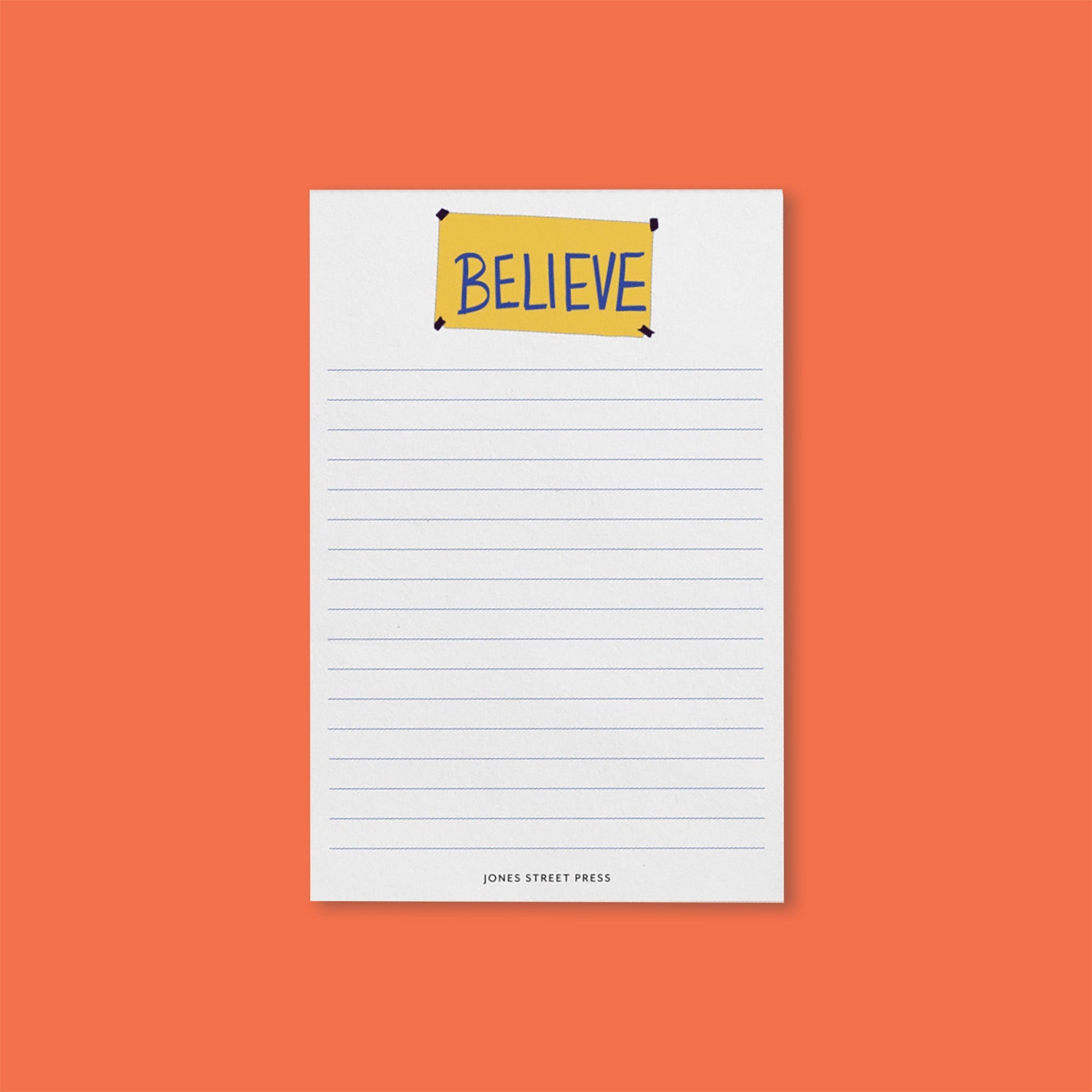 On an orangey-red background sits a notepad. This Ted Lasso inspired white notepad has blue lines on it with an illustration of a yellow "BELIEVE" banner.