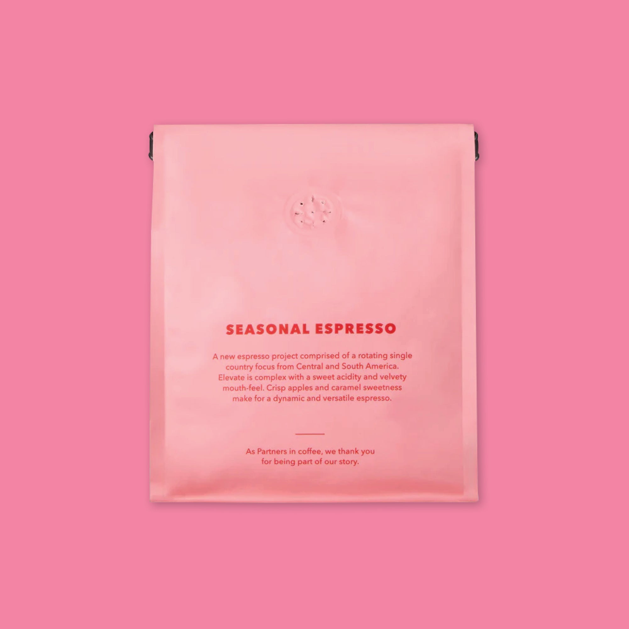 On an bubblegum pink background is a photo of the back of a pink and red bag of Partners Coffee Roasters Brooklyn - New York Jumpstart Blend. It says, "SEASONAL ESPRESSO: A new espresso project comprised of a rotating single country focus from Central and South America. Elevate is complex with a sweet acidity and velvety mouth feel. Crisp apples and caramel sweetness make for a dynamic and versitile espresso. As Partners in coffee, we thank you for being a part of our story."