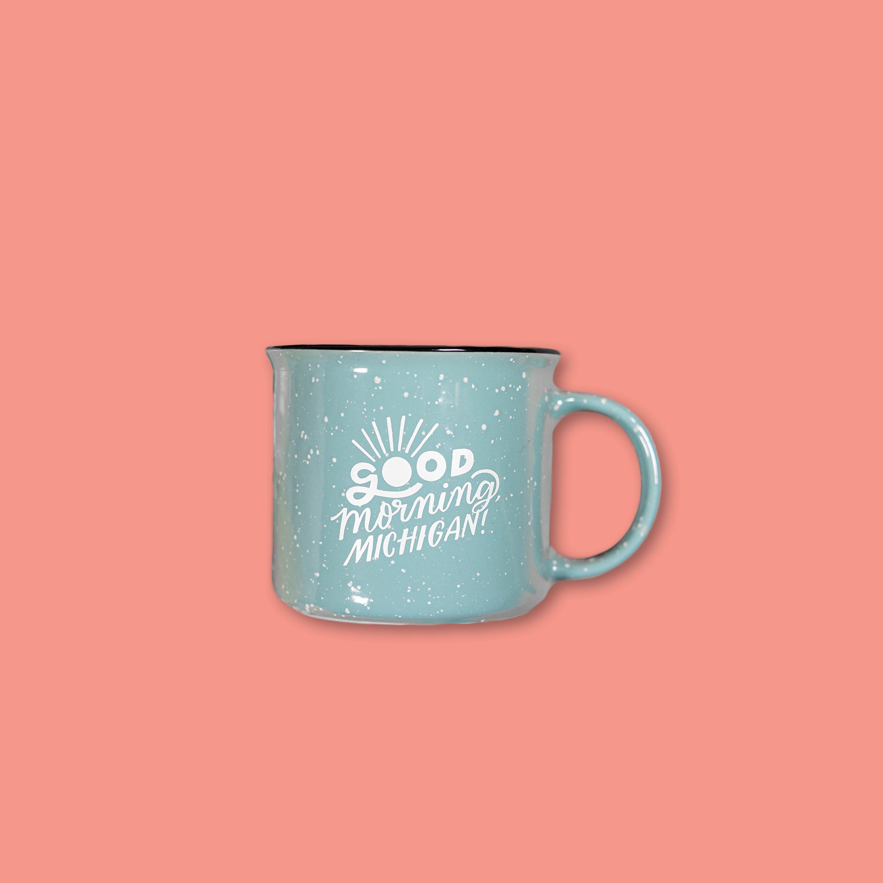 On a coral background sits a 15 oz. light teal campfire mug with "Good morning Michigan" in white writing.