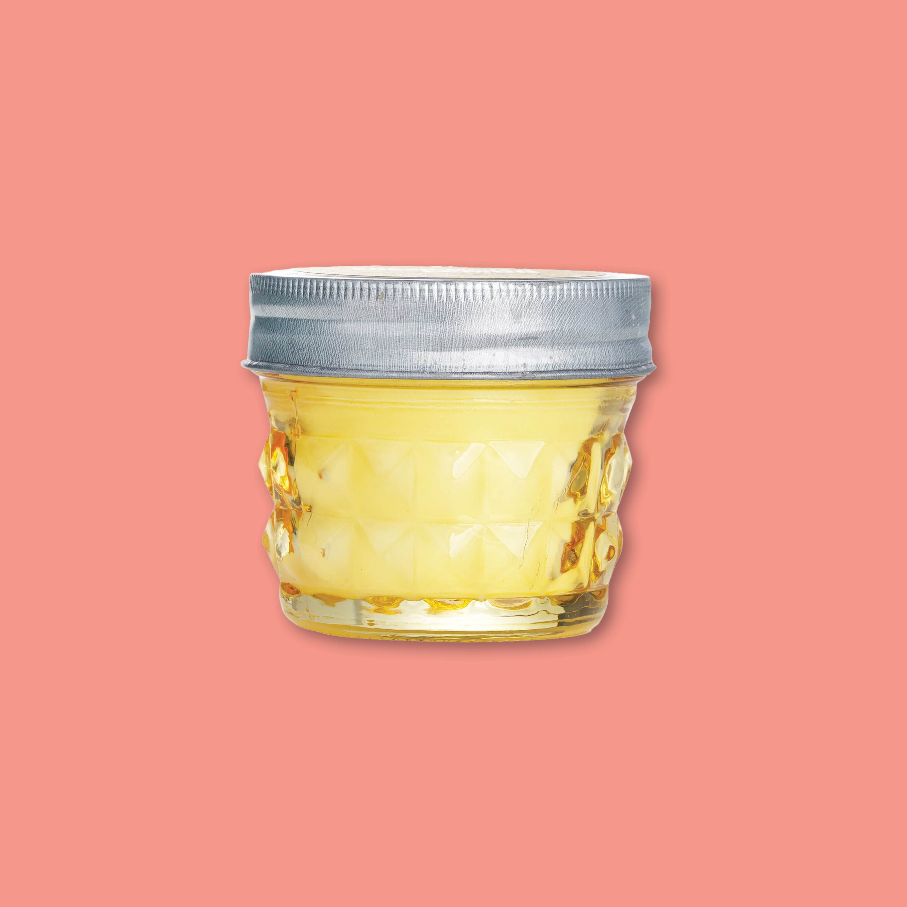 On a coral background sits a 4 oz. yellow glass Paddywax Fresh Meyer Lemon candle with tin lid.