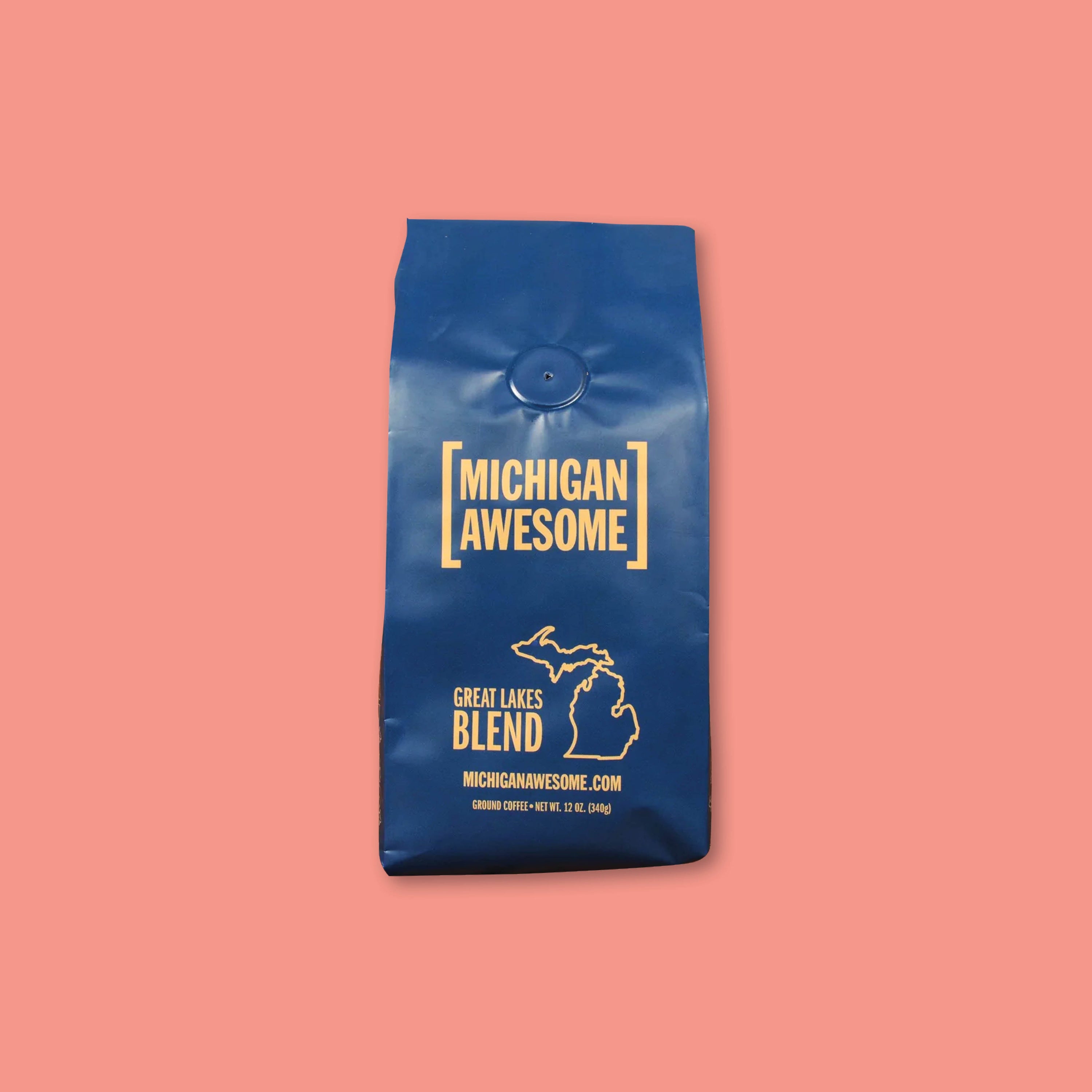 On a coral background sits a 12 oz. navy blue bag of Great Lakes Blend coffee from Michigan Awesome.