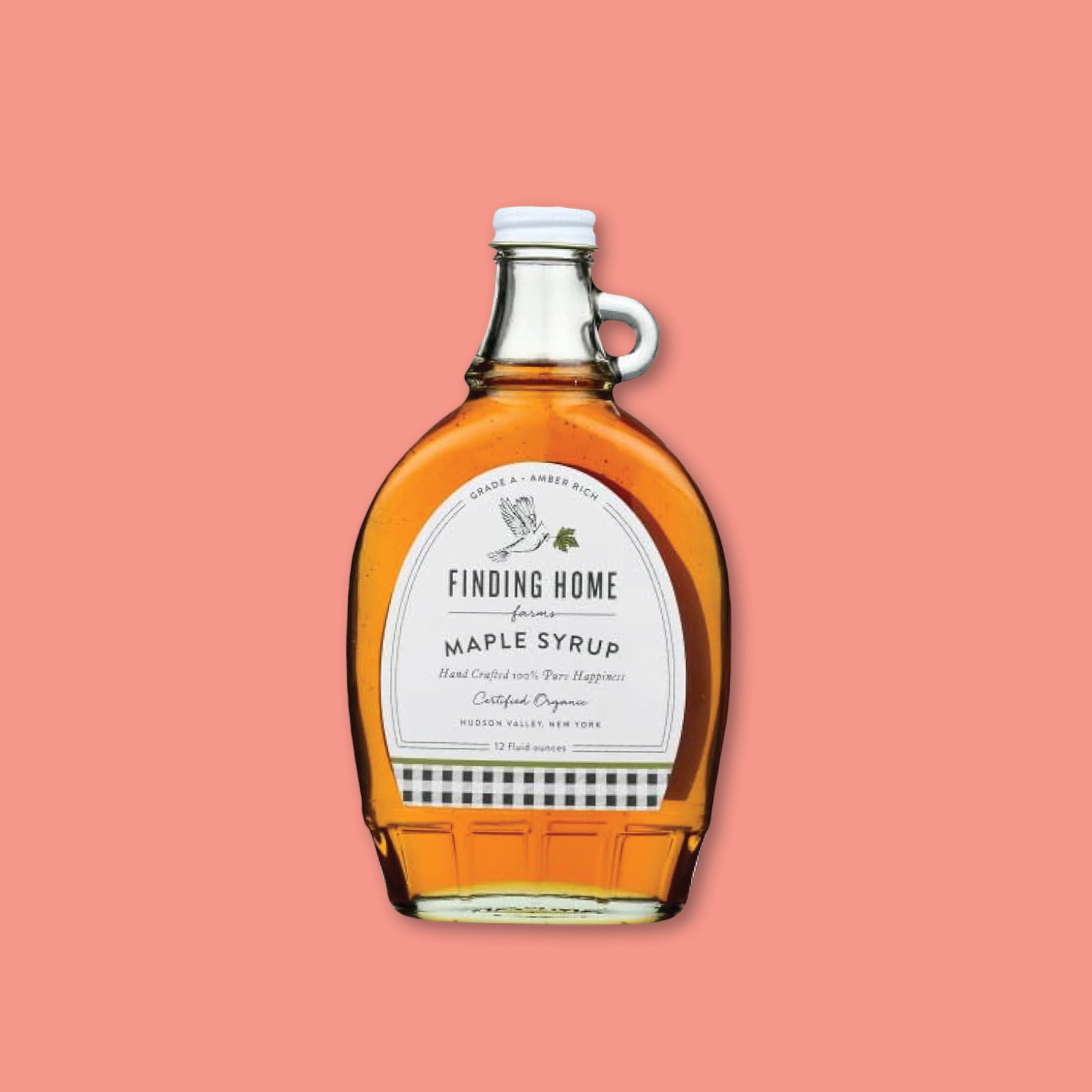 On a coral background sits a 12 oz. glass bottle of Finding Home Maple Syrup.