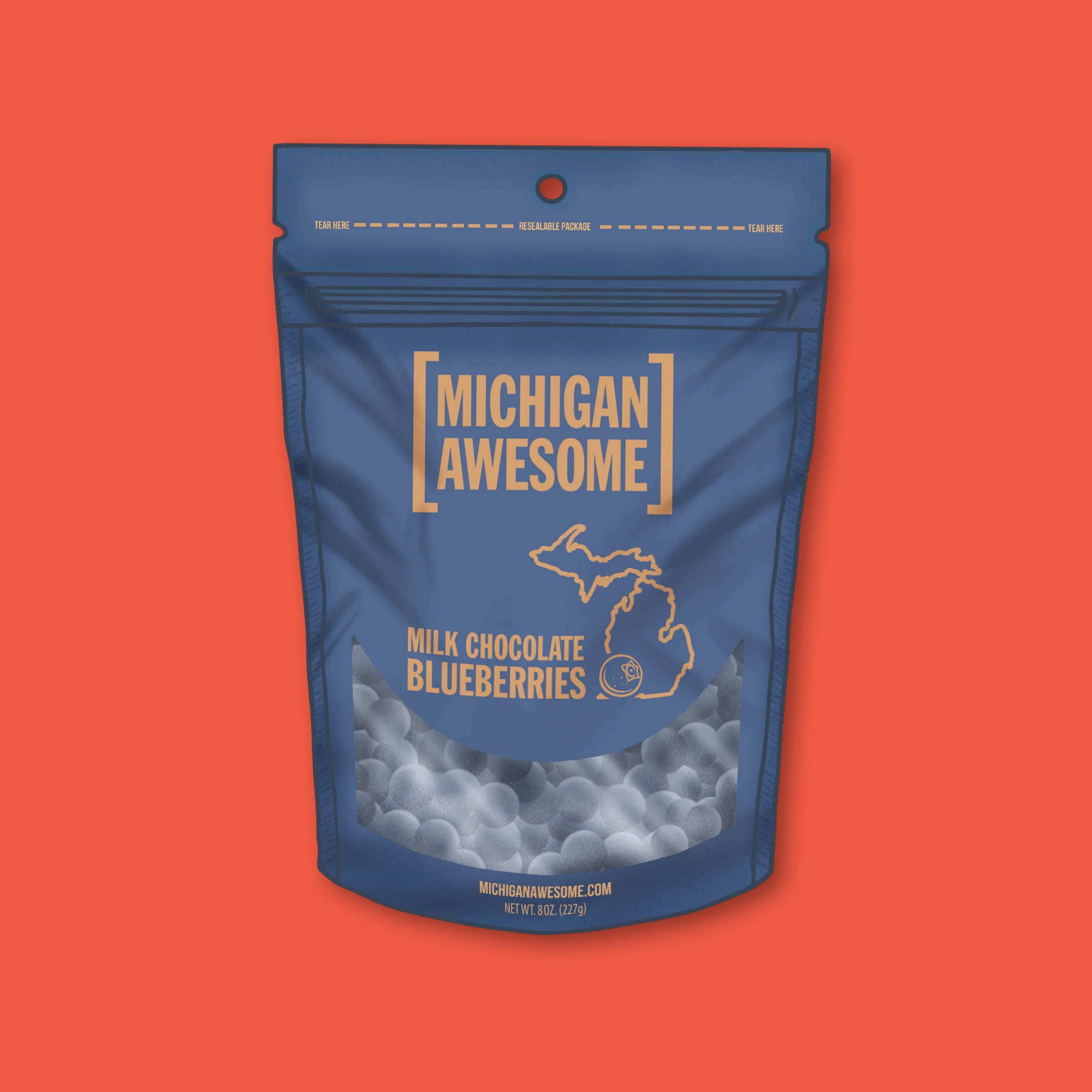 On a tomato red background sits a an 8 oz. navy blue pouch of Milk Chocolate Blueberries from Michigan Awesome.