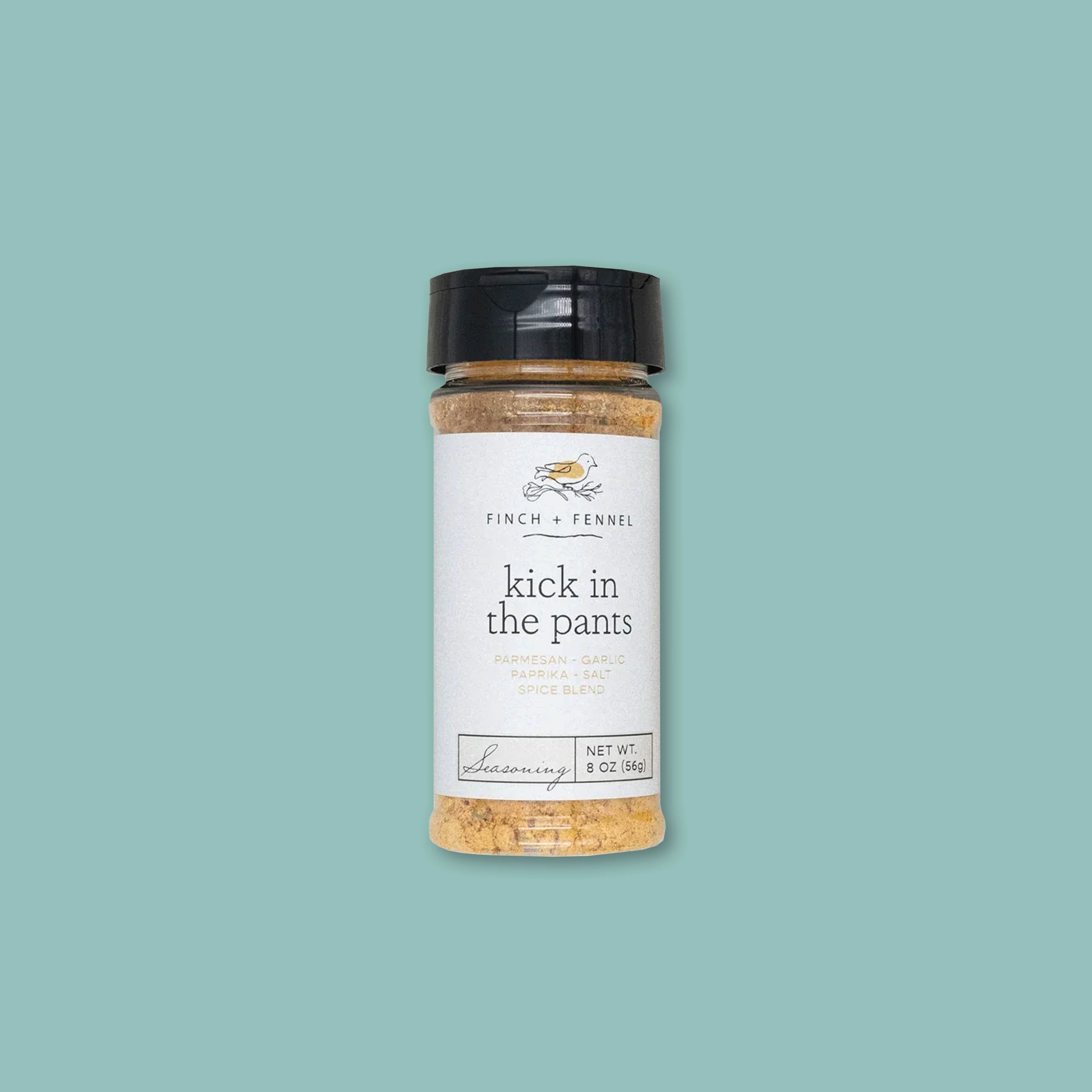 On a teal background sits a jar of Kick in the Pants spice blend from Finch + Fennel with a black lid.