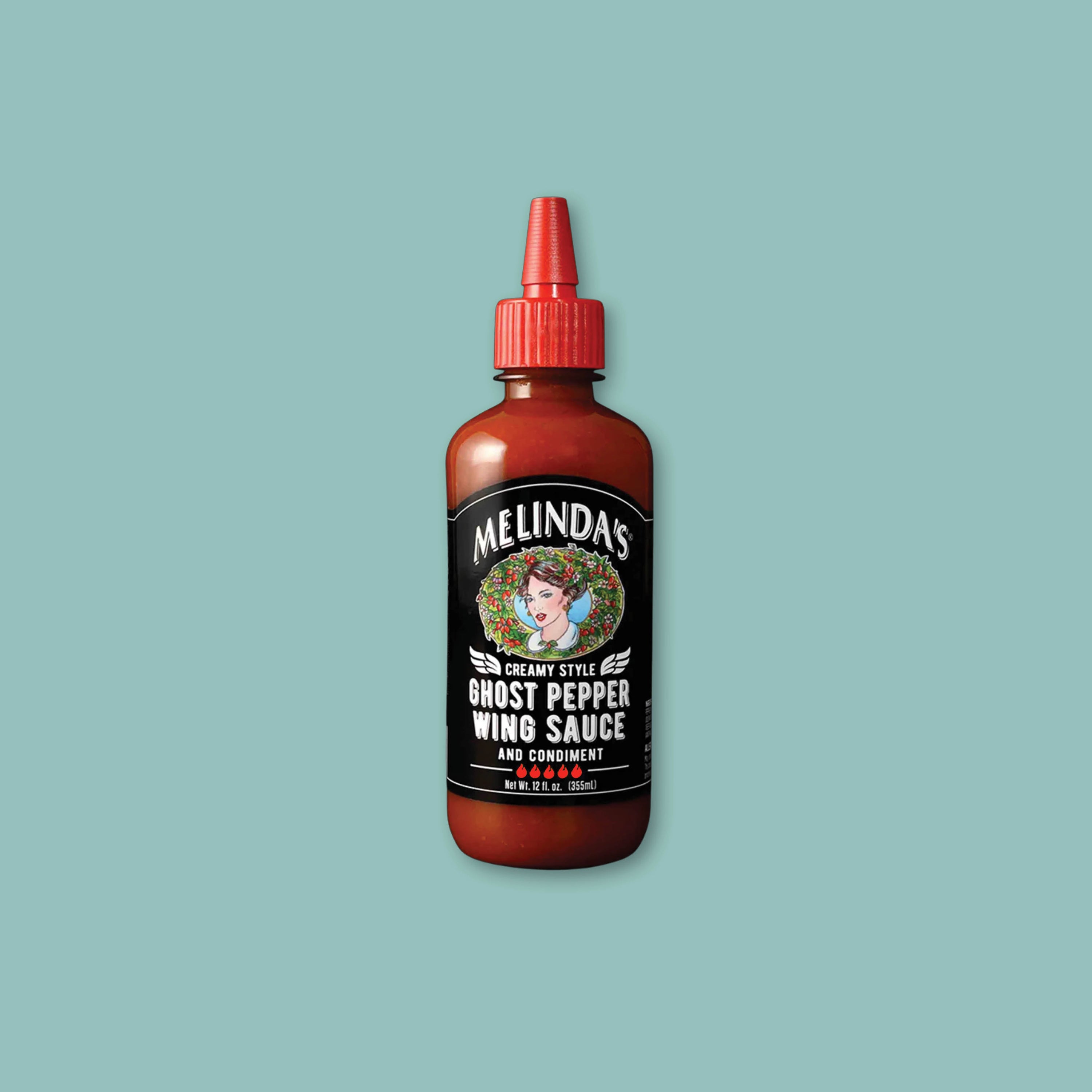 On a teal background sits a bottle of Melinda's Creamy Style Ghost Pepper Wing Sauce with a red spout lid.
