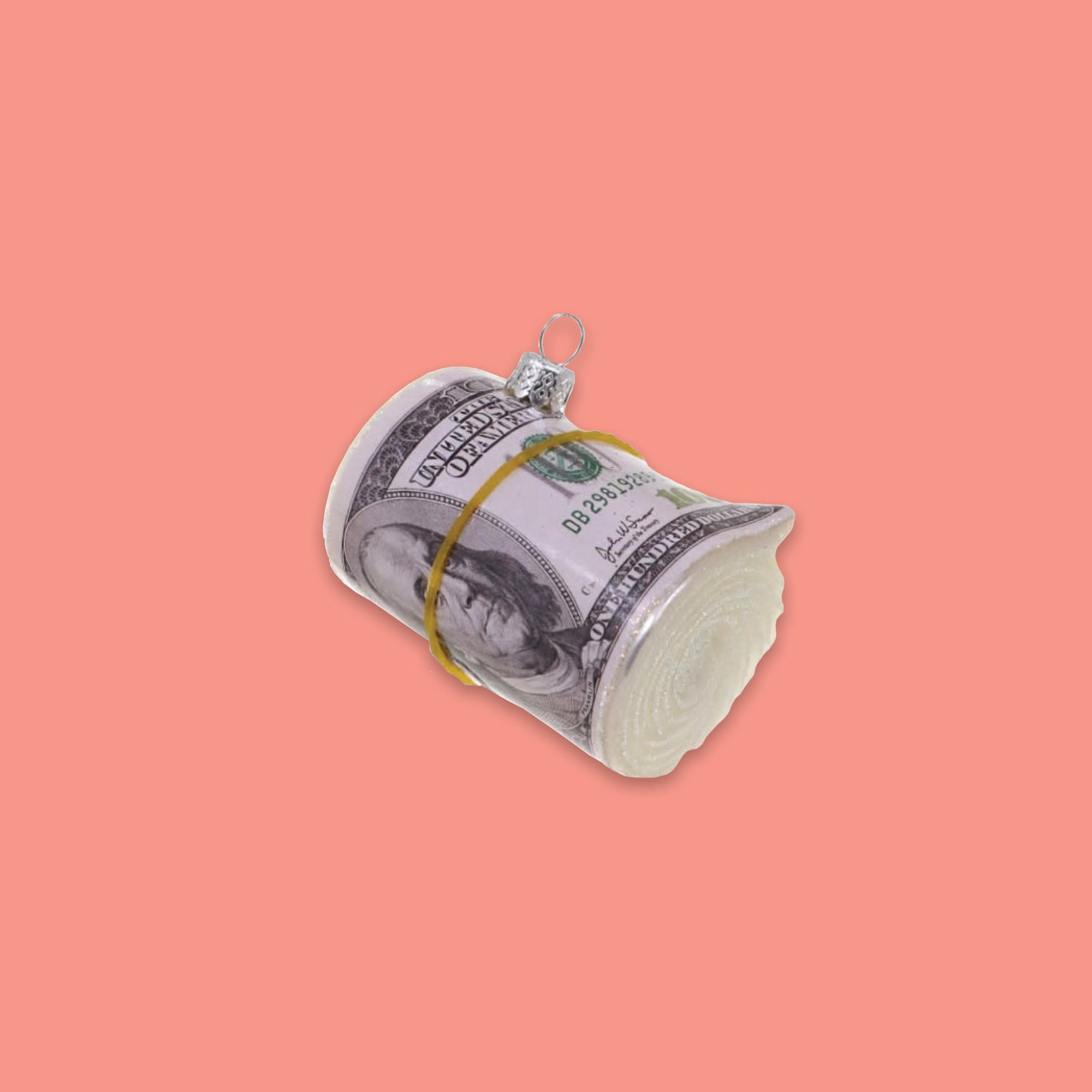 On a coral pink background sits a glass ornament of a roll of cash held by a rubberband.