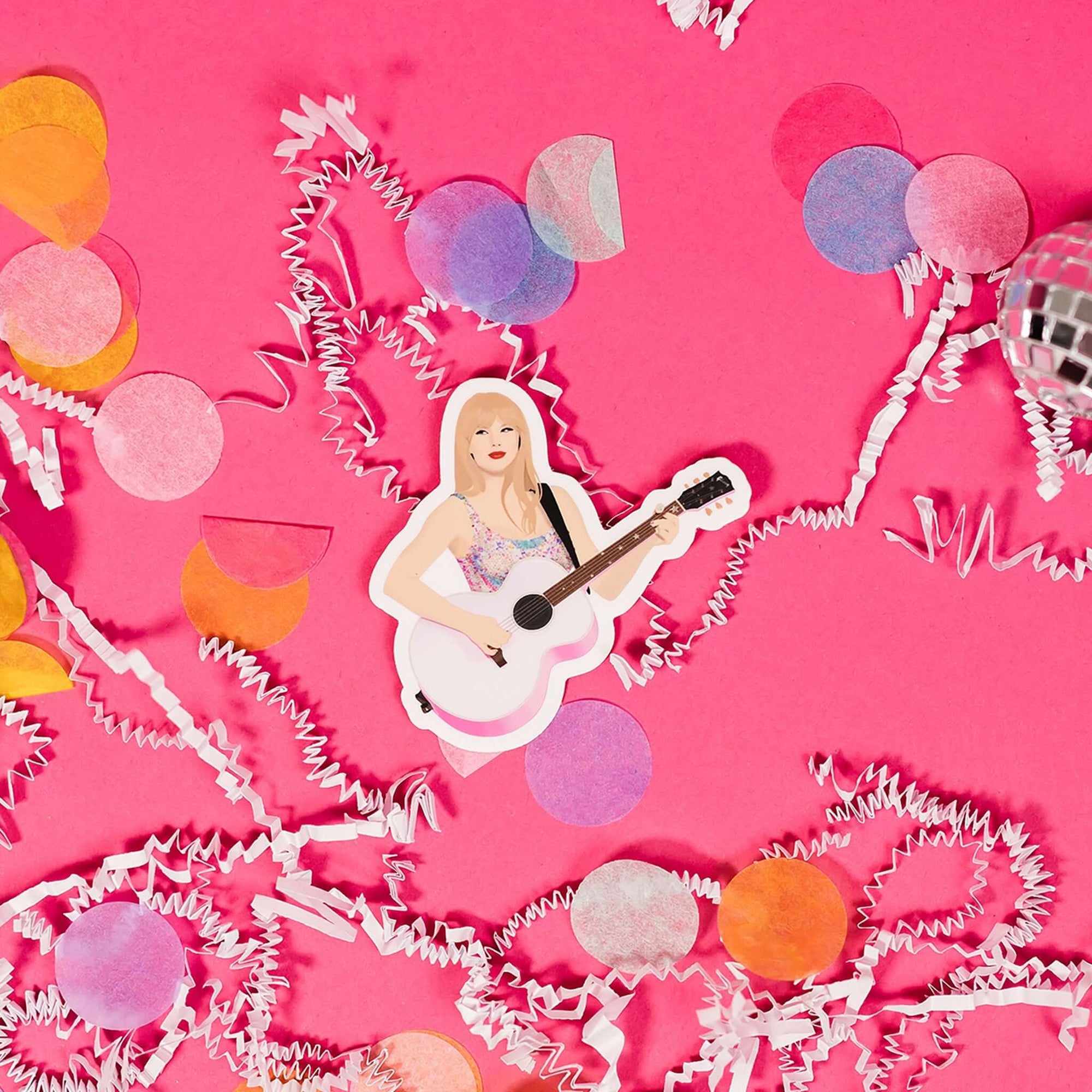 On a hot pink background sits a sticker with white crinkle and big, colorful confetti scattered around. This Taylor Swift inspired sticker is an illustration of Taylor Swift holding a pink guitar.