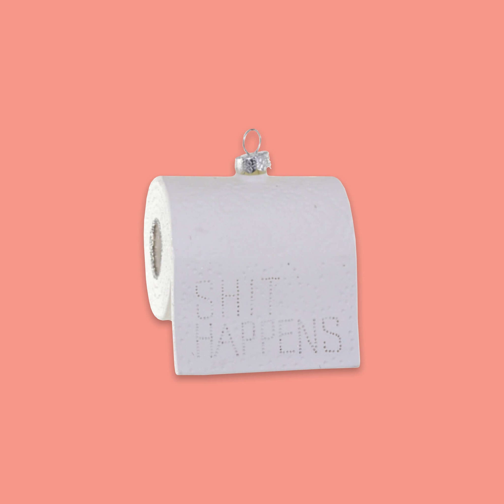 On a coral pink background sits an ornament. This glass ornament is of a white toilet paper roll and it says "SHIT HAPPENS" in punched out letters.