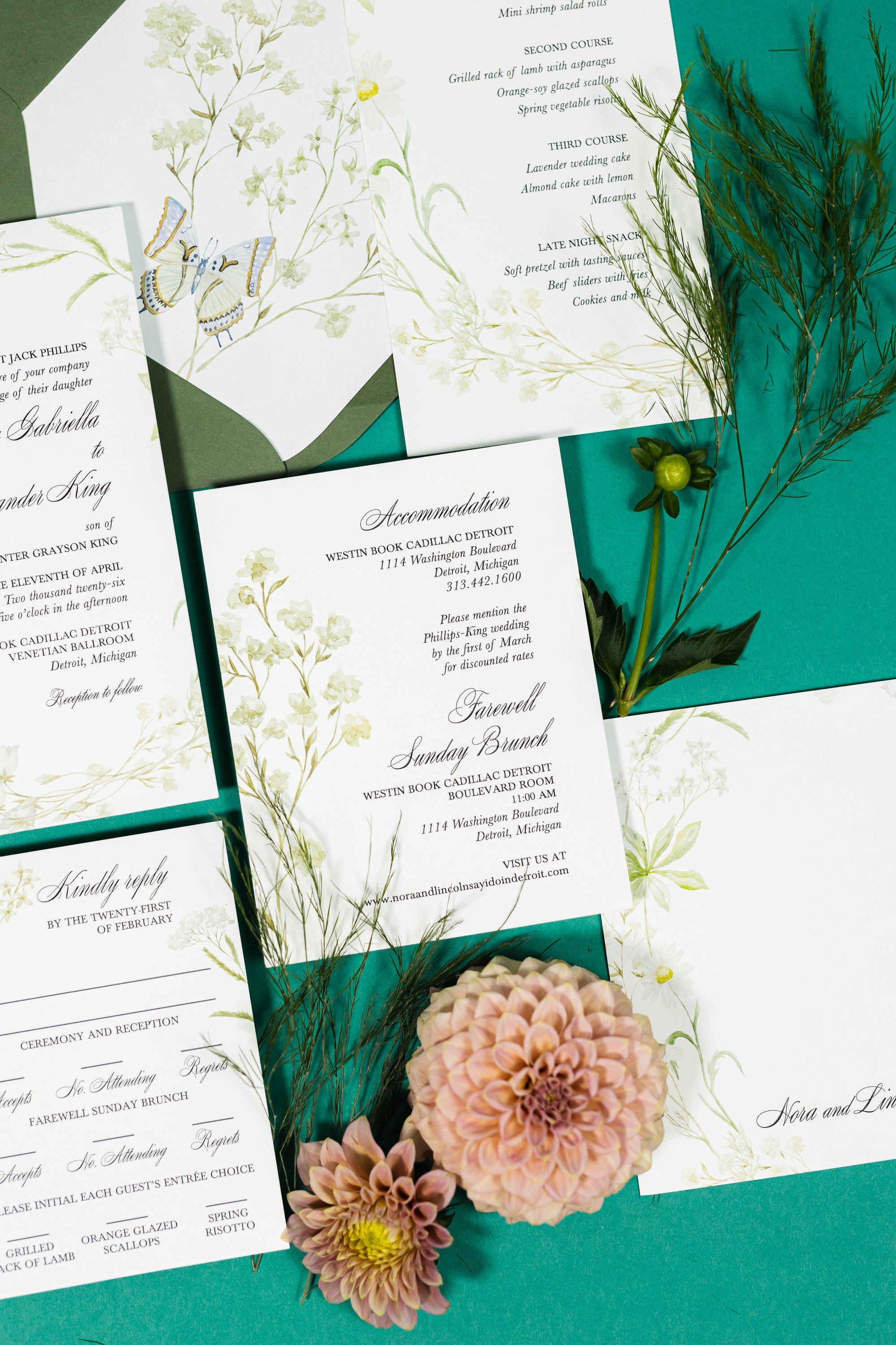 On a teal background is a flat lay of a romantic sample wedding invitation suite with script and olive green floral illustration accents