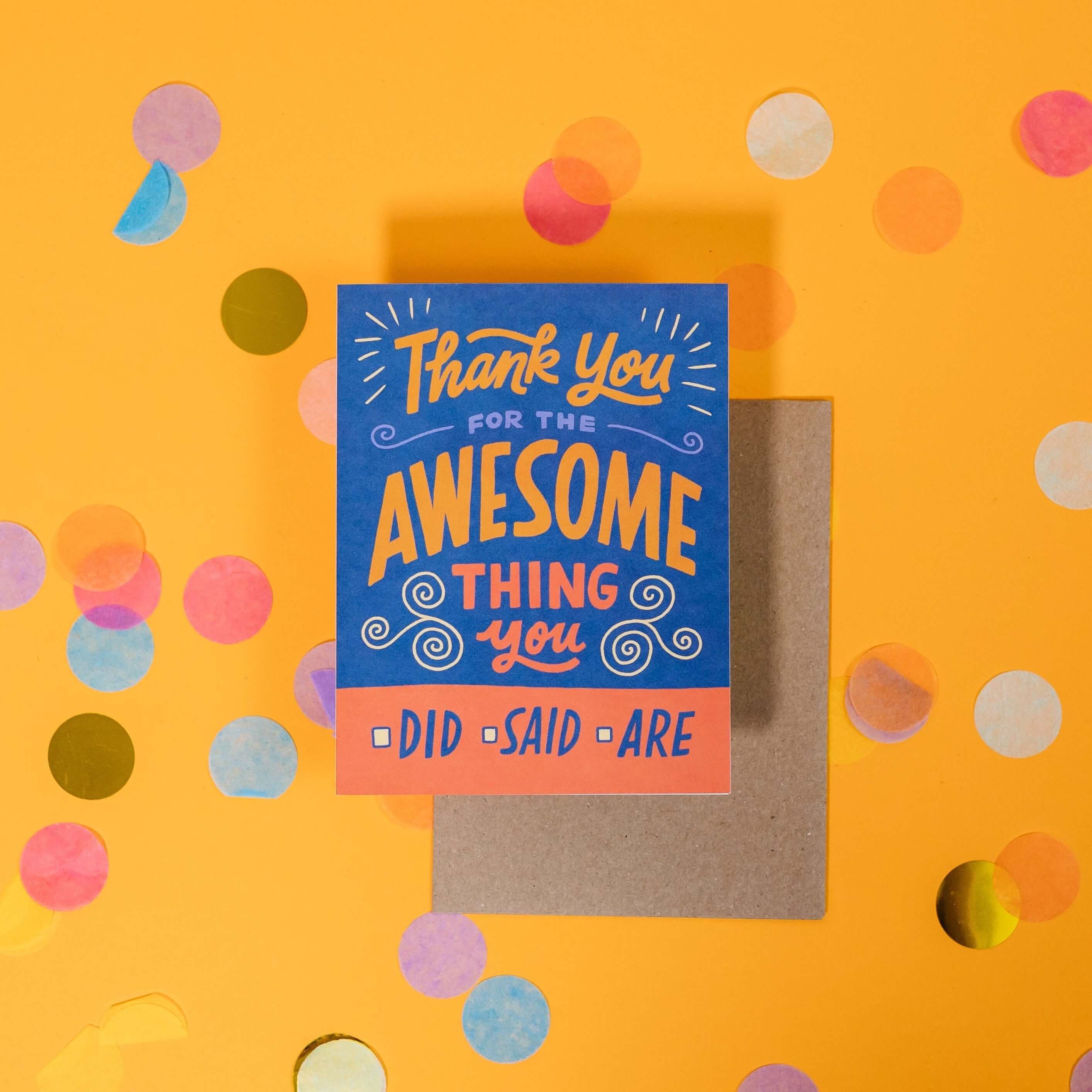 On a sunny mustard background is a greeting card and envelope with big, colorful confetti scattered around. The blue and orange greeting card says "Thank You For The Awesome Thing You" in handwritten sunny mustard, orange, and blue lettering. Under that has a squre in front of the words "Did," "Said," "Are" handwritten in blue lettering. The kraft envelope sits under the card. 