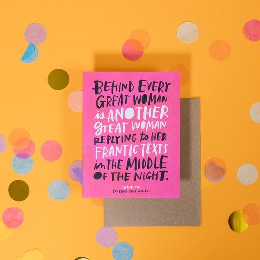 On a sunny mustard background is a greeting card and envelope with big, colorful confetti scattered around. The hot pink greeting card has handwritten letterpress text in black and white that says "Behind Every Great Woman is Another Great Woman Replying to Her Frantic Texts in the Middle of the Night. Thank You for Being That Woman." The kraft envelope sits under the card. 