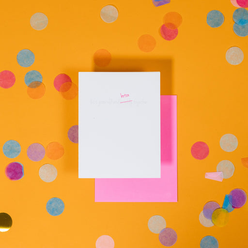 On a sunny mustard background is a greeting card and envelope with big, colorful confetti scattered around. The white greeting card says "let's grow old and wrinkly together" in handwritten grey letterpress and the word "wrinkly" is crossed out with a hot pink line and above it says "botox" in hot pink handwritten lettering. The hot pink envelope sits under the card. 