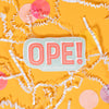 On a sunny mustard background sits a sticker with white crinkle and big, colorful confetti scattered around. This mint blue sticker says "OPE!" in handwritten vintage red block lettering and white skinny handwritten lettering on top, with a white dropshadow. Under it says "Rock Paper Scissors" in white handwritten script lettering. 2"-3"