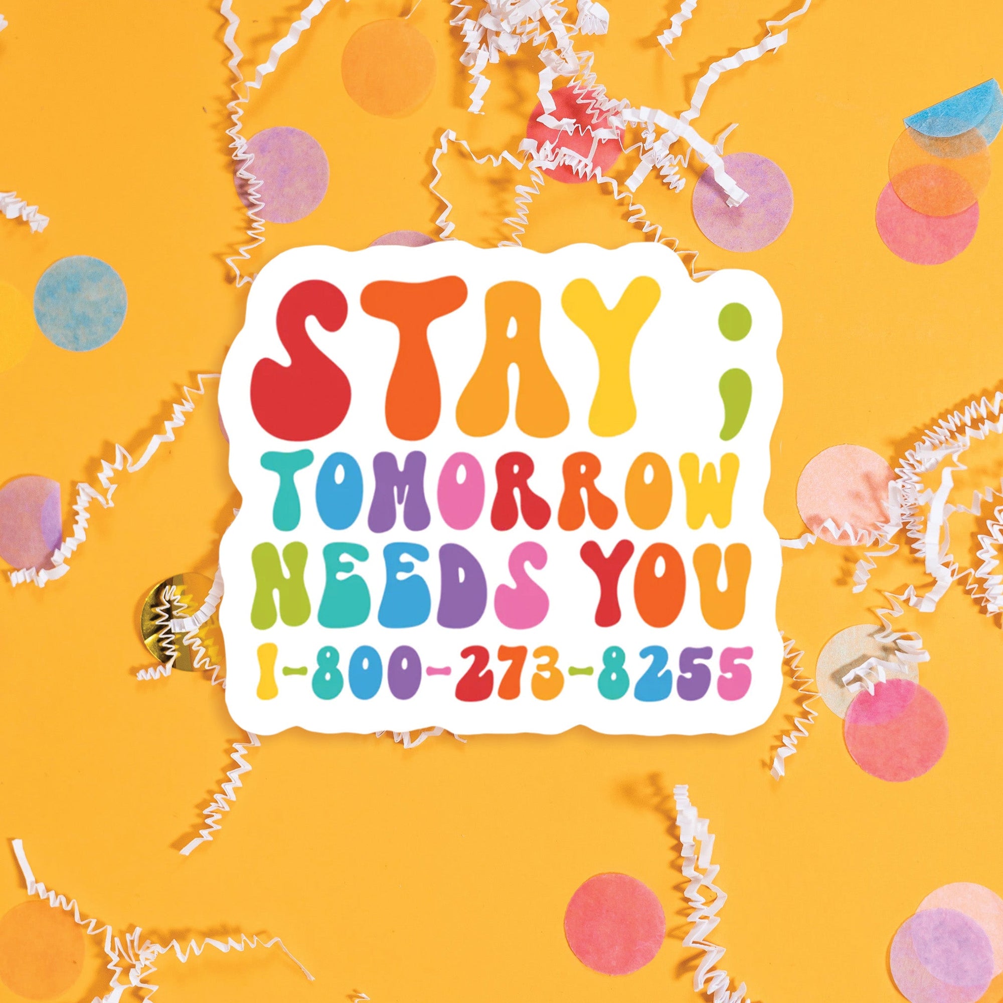 On a sunny mustard background sits a sticker with colorful confetti and white crinkle scattered around. This sticker has colorful lettering in red, dark coral, orange, sunny mustard, celery green, turquoise, blue, purple, and bubblegum pink. It says "STAY; TOMORROW NEEDS YOU 1-800-273-8255" in thick serif font. Approximately 3".