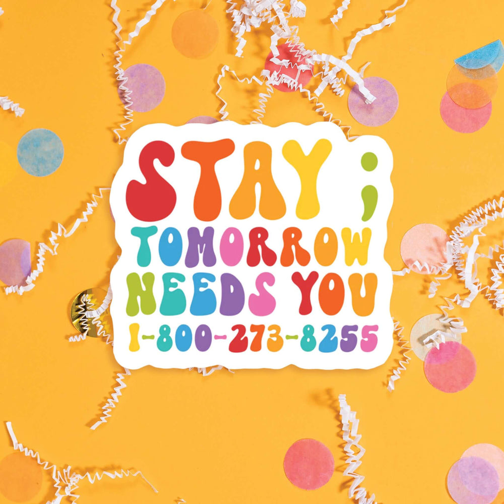 On a sunny mustard background sits a sticker with colorful confetti and white crinkle scattered around. This sticker has colorful lettering in red, dark coral, orange, sunny mustard, celery green, turquoise, blue, purple, and bubblegum pink. It says "STAY; TOMORROW NEEDS YOU 1-800-273-8255" in thick serif font. Approximately 3".