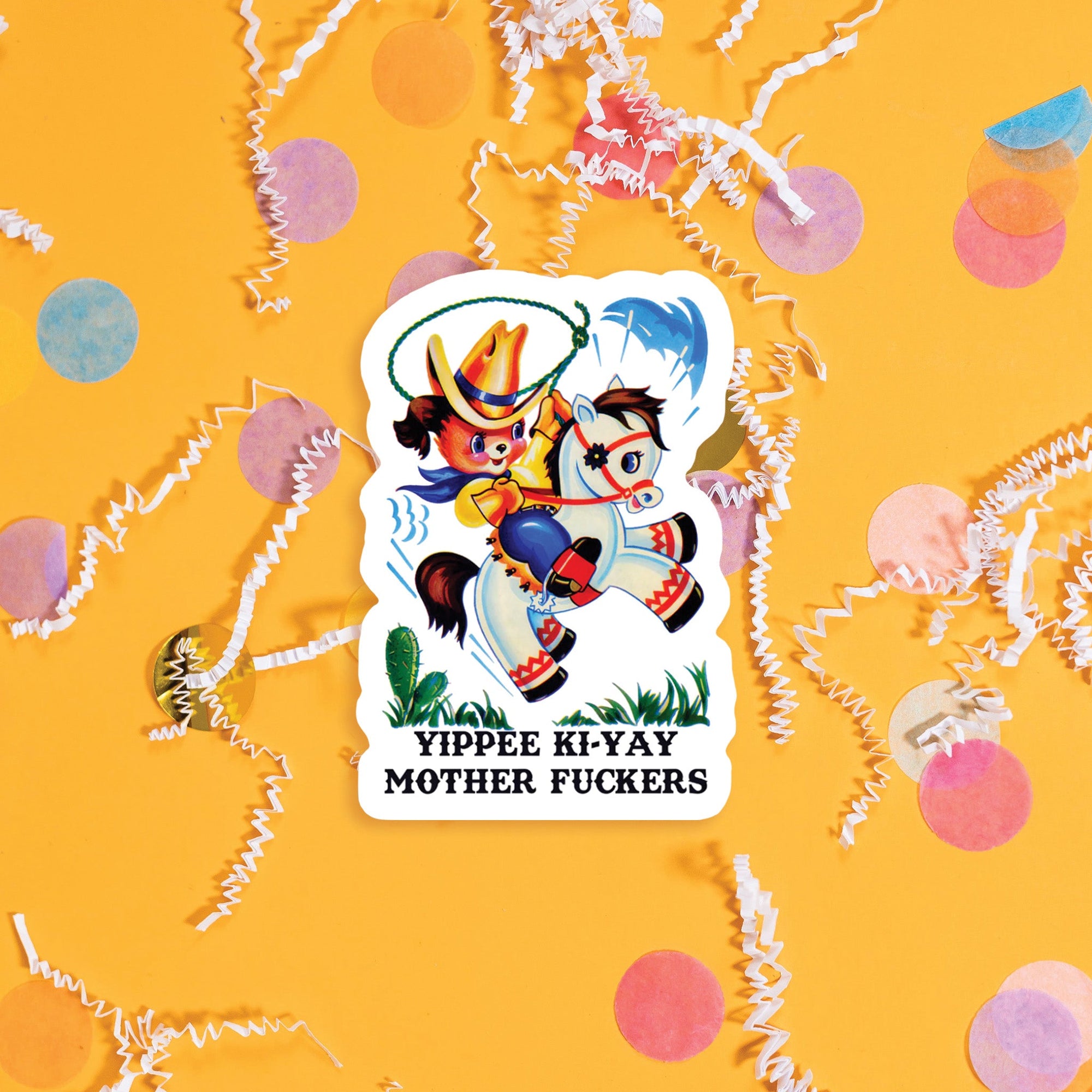 On a sunny mustard background sits a sticker with colorful confetti and white crinkle scattered around. This vintage sticker has an illustration of a cute brown puppy riding a white pony with a lasso in it's hand It is dressed as a cowboy. It says "YIPPEE KI-YAY MOTHER FUCKERS" in black, all caps western font. Approximately 3".