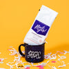 On a sunny mustard background sits a mug and a bag of coffee with white crinkle and big, colorful confetti scattered around.  The navy campfire mug has white specks and says "Ann Arbor" in a white, handwritten script lettering font. The white bag of coffee sits atop the mug. The coffee is Rock Paper Scissors 'Hail Yes!' in white hand lettering on a brilliant blue label. It is 'BLUEBERRY CRUMBLE GROUND COFFEE'. Small batch roasted, fruit forward, balanced w/ aromatic vanilla. Net Wt. 12 oz. (340g)