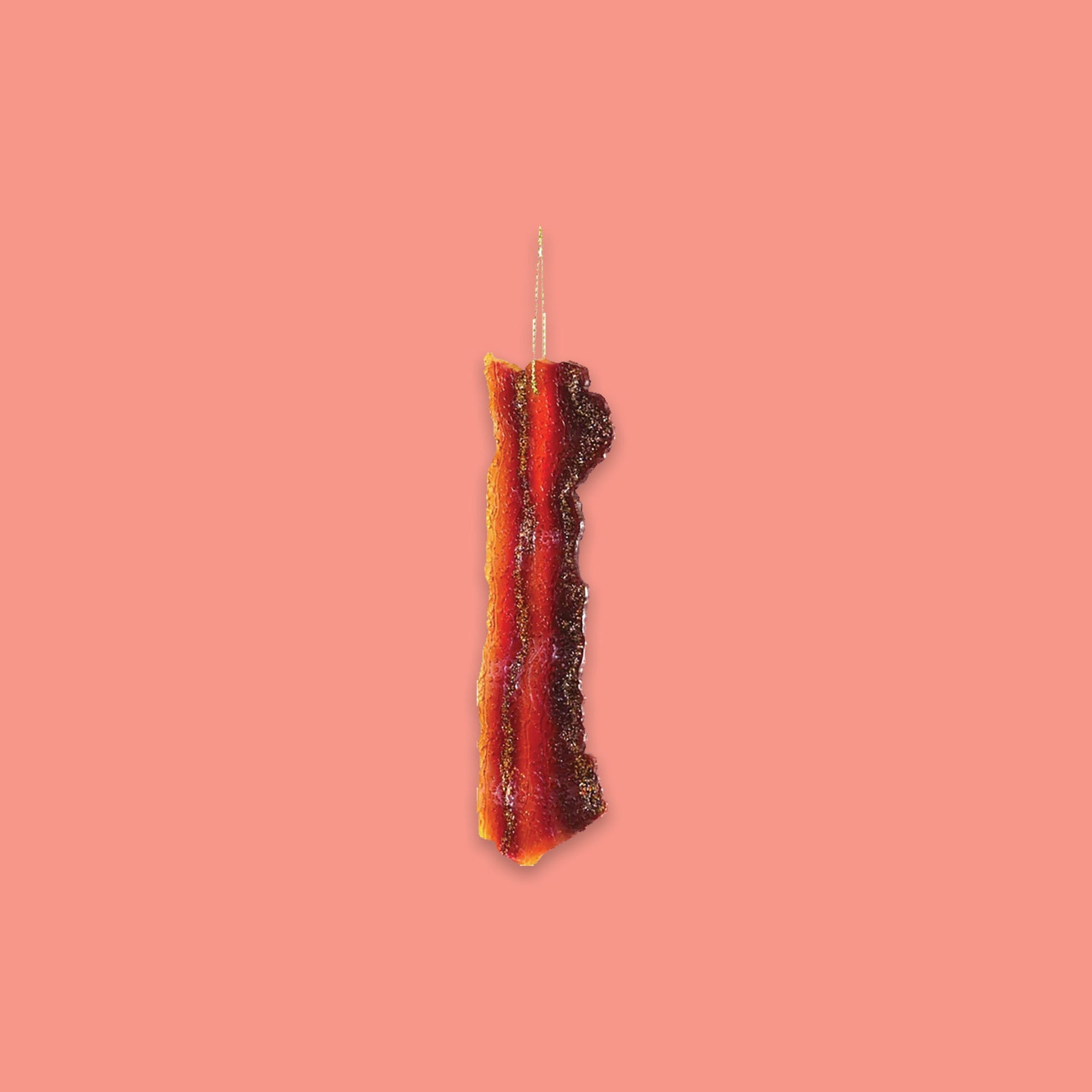 On a coral pink background sits a slice of bacon ornament. This glass ornament looks like a real bacon slice!