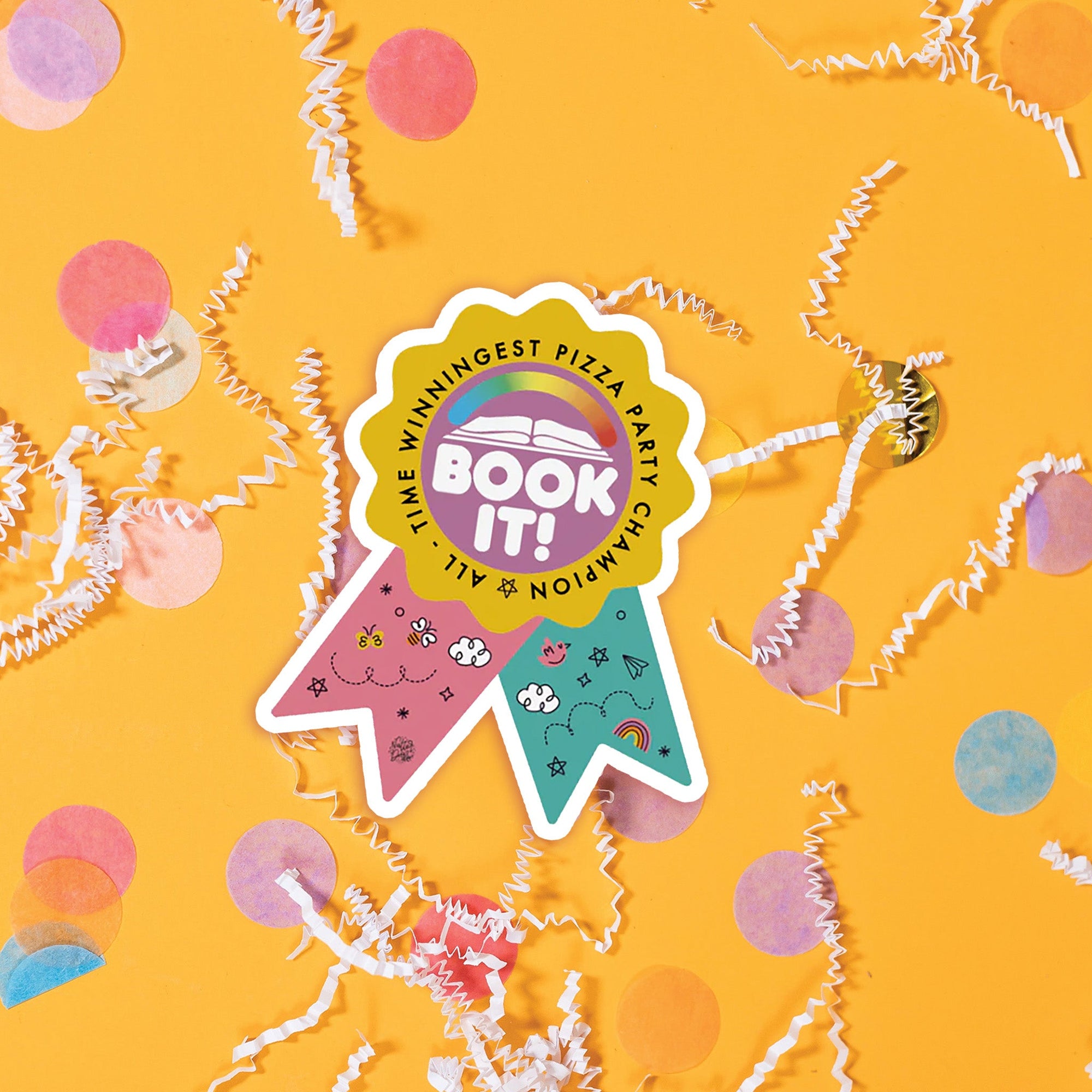 On a sunny mustard background sits a sticker with white crinkle and big, colorful confetti scattered around. This colorful ribbon sticker has an illustration of an open book and a rainbow meter above it. It says "BOOK IT!" in a white, bubble text. There are handdrawn doodles on the pink and turquoise ribbons. 'ALL-TIME WINNINGEST PIZZA PARTY CHAMPION'.