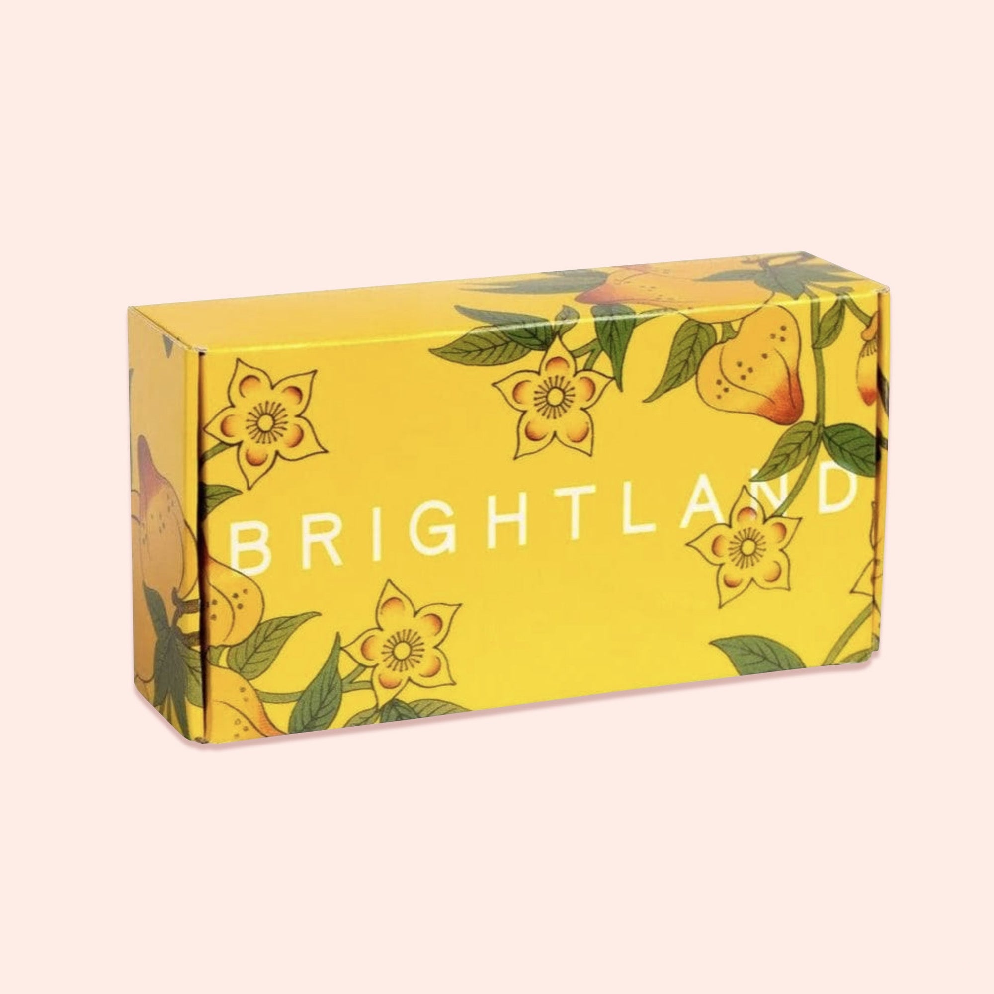 On a light pink background sits an BOX. This yellow box has colorful illustrations of flowers and leaves it says "BRIGHTLAND" in white lettering.