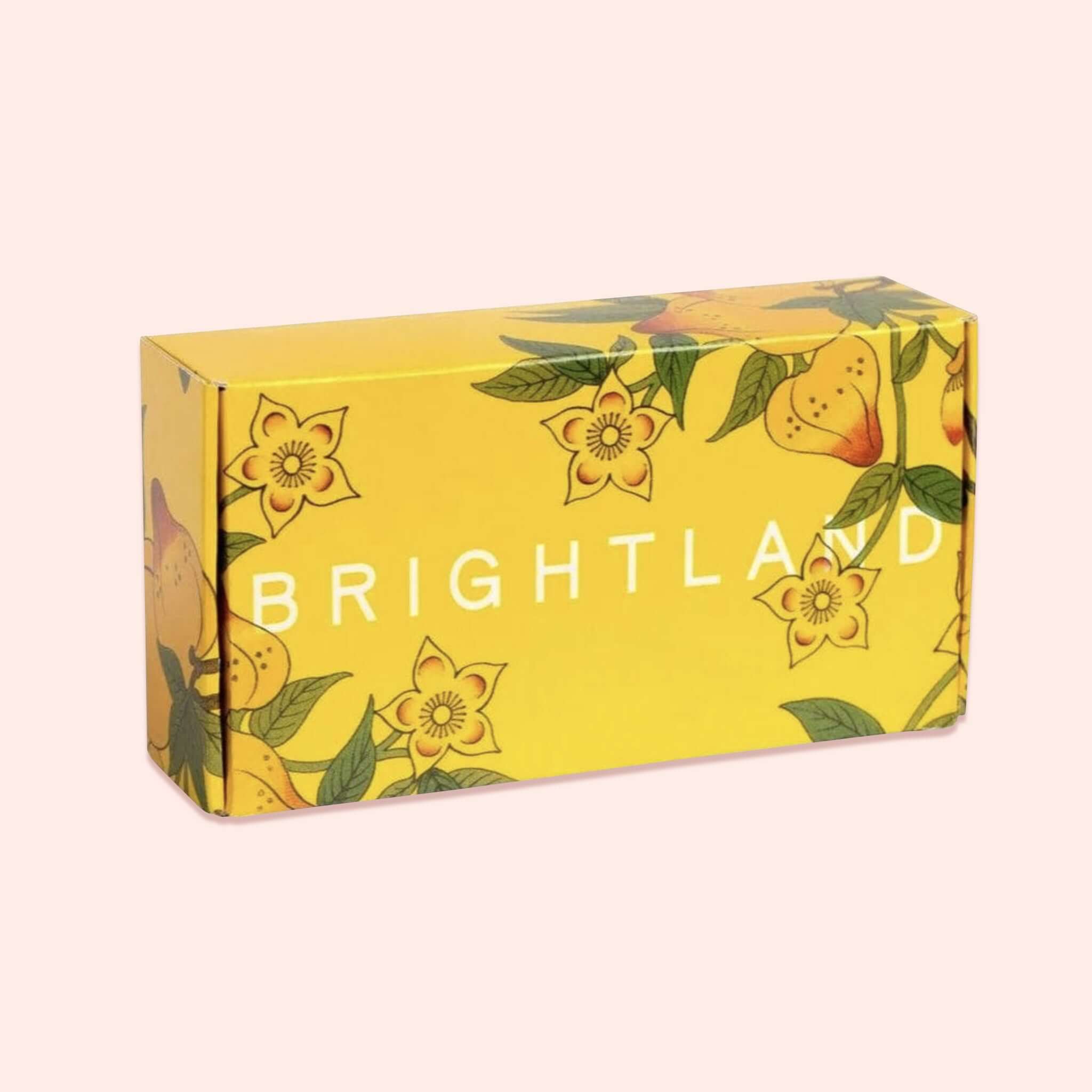 On a light pink background sits an BOX. This yellow box has colorful illustrations of flowers and leaves it says "BRIGHTLAND" in white lettering.