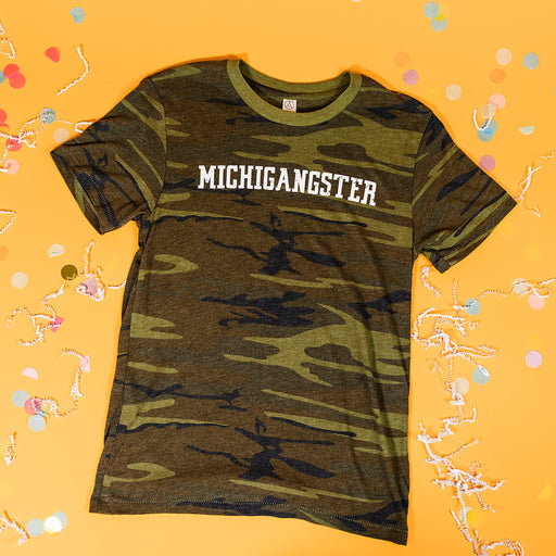 On a sunny mustard background sits a t-shirt with white crinkle and big, colorful confetti scattered around. This camo tee features "MICHIGANGSTER" in a distressed, varsity-style white print.