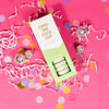 On a hot pink background sits an opened box with white crinkle and big, colorful confetti scattered around. There are mini disco balls. This picture is a close-up of a white and pistachio green package that says "CHILL THE FUCK OUT" in gold foil, all caps block lettering. Under it says "set of 8" and " shower steamers" in grey, lowercase serif font. At the bottom it says "eucalyptus" in gold foil, lower case serif font. The box is opened to reveal the pistachio green shower steamers in it. 