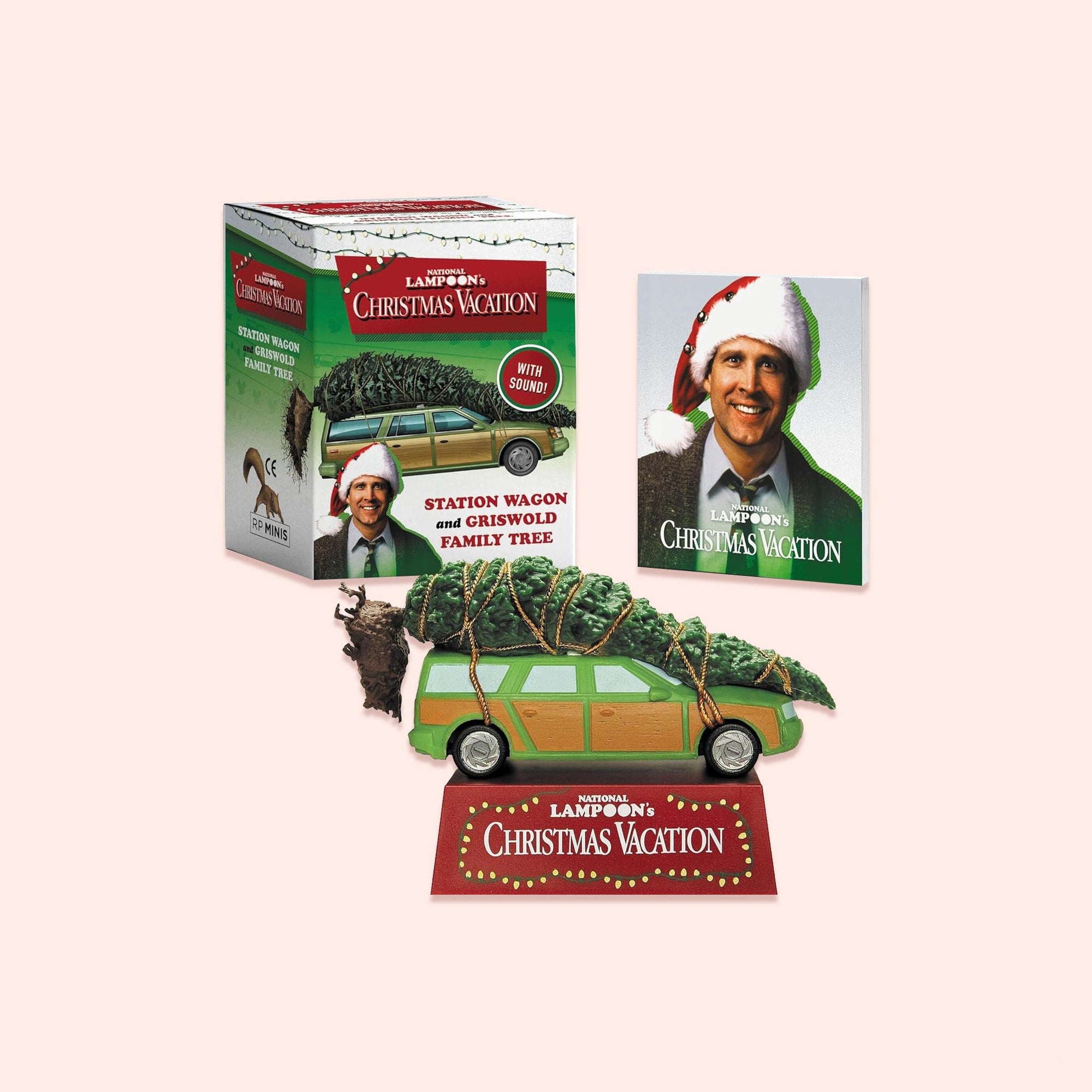 On a light pink background sits a Christmas Vacation inspired kit is of a stationwagon with a christmas tree tied to the top and a box behind it. There is a picture of Clark in a santa hat. 