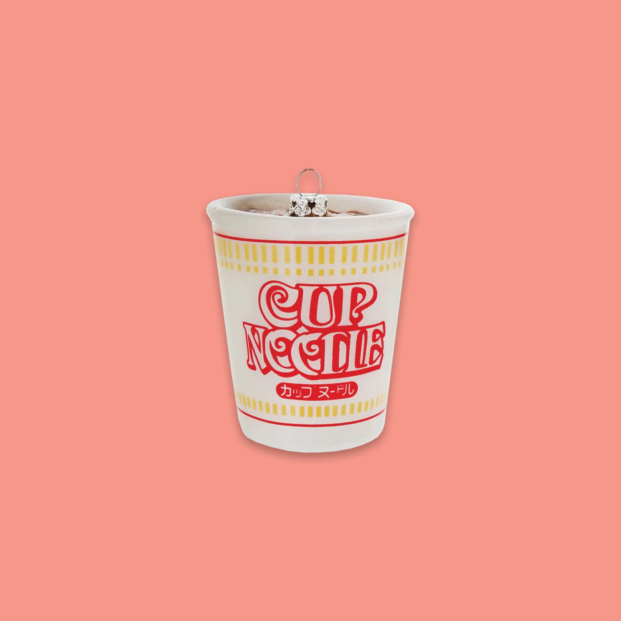 On a coral pink background sits a cup ornament. This is a white glass 'CUP NOODLE' ornament with chinese writing, and red and yellow lines. 