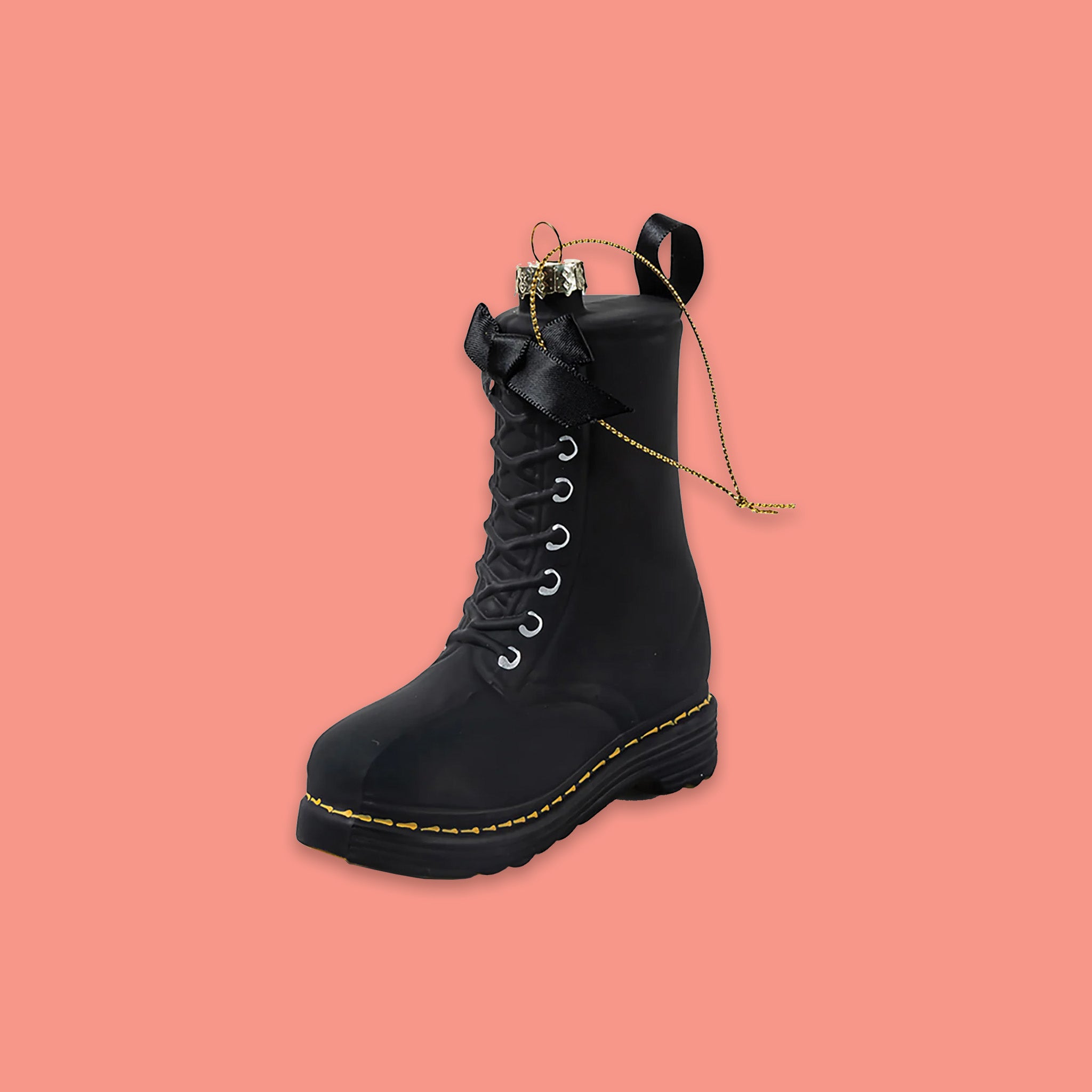 On a coral pink background sits a boot ornament. This is a black glass Doc Martens boot with yellow stitching.