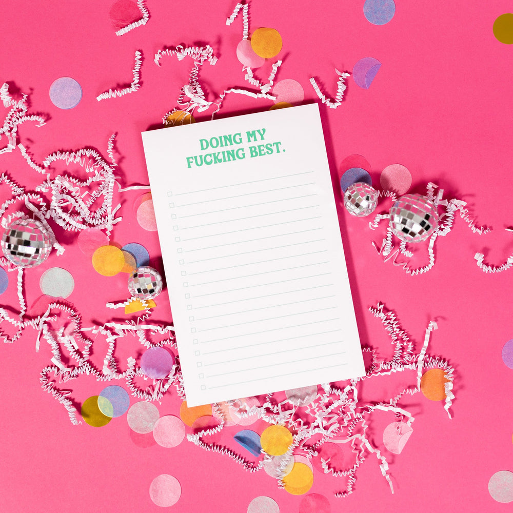On a hot pink background sits a notepad with white crinkle and big, colorful confetti scattered around. There are mini disco balls. There is a white notepad with "DOING MY FUCKING BEST." at the top. It is in a blue green color in a groovy font. There are check boxes and lines.