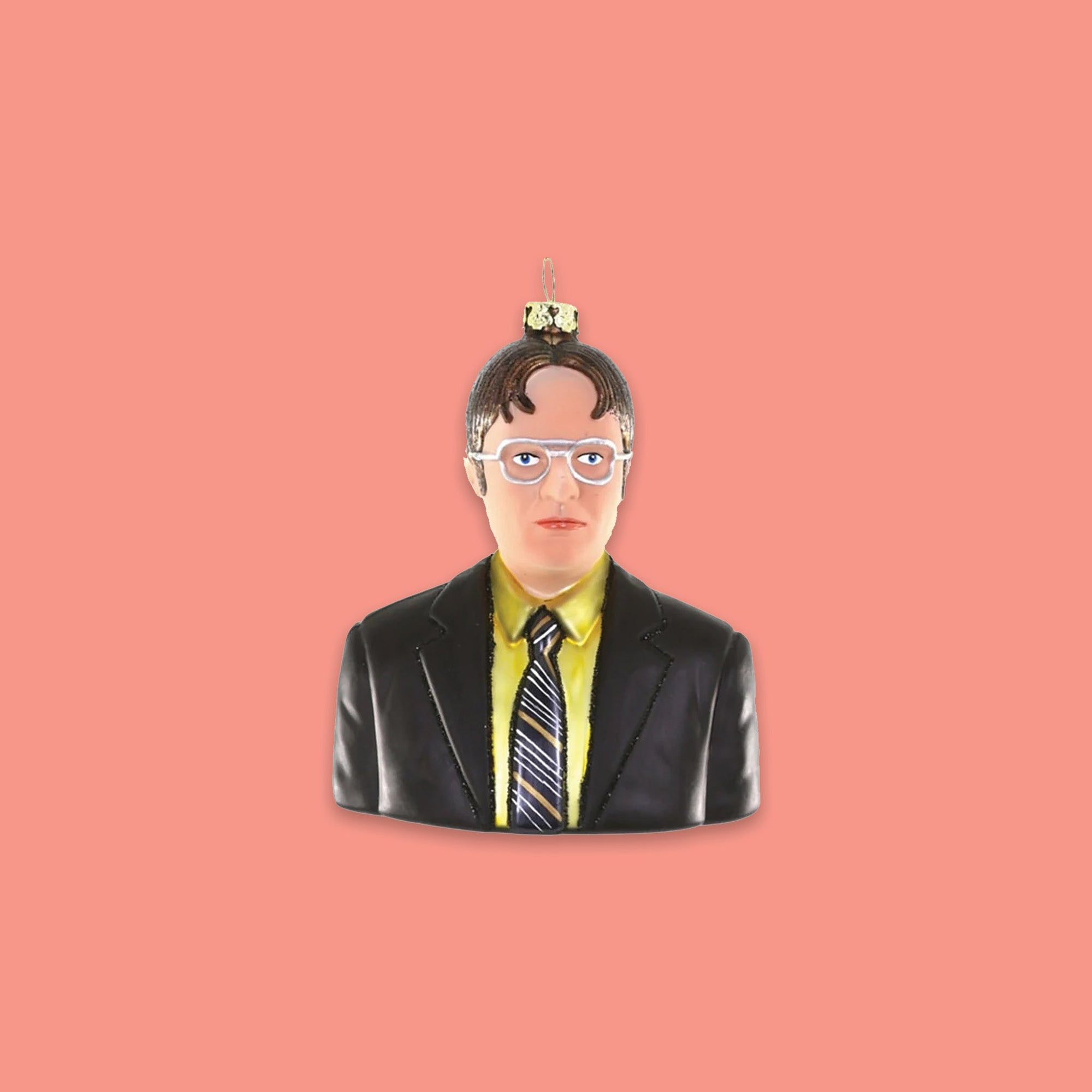 On a coral pink background sits an ornament. The Office inspired glass ornament is a bust of Dwight Schrute wearing a yellow shirt, a tie, and a jacket. He has on silver glasses.