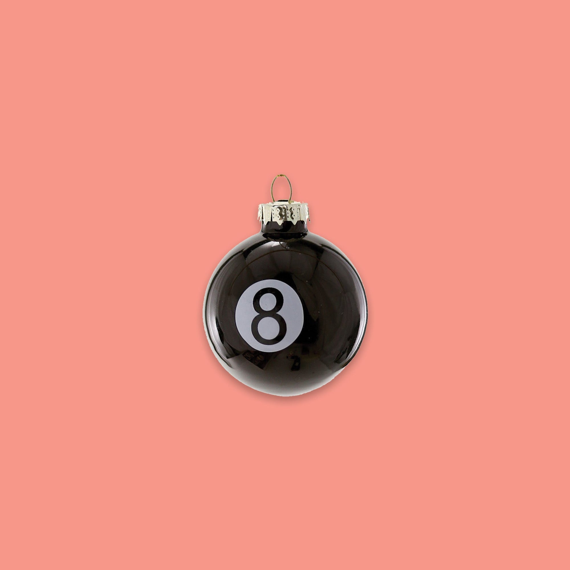 On a coral pink background sits a ball ornament. This is a glass 'Eight Ball' black ornament with a white dot and the number 8 on it in black.