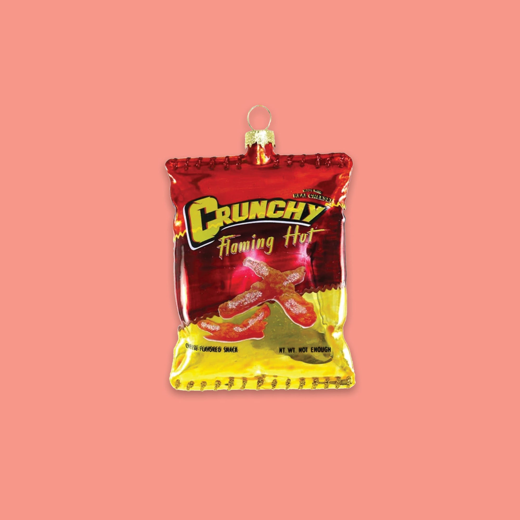 On a coral pink background sits a chip bag ornament. This red and yellow glass 'Crunchy Flaming Hot' ornament looks like a real bag of chips and has cheetos chips on the front. It says on the bottom "CHEESE FLAVORED SNACK" and "NET WT NOT ENOUGH." 