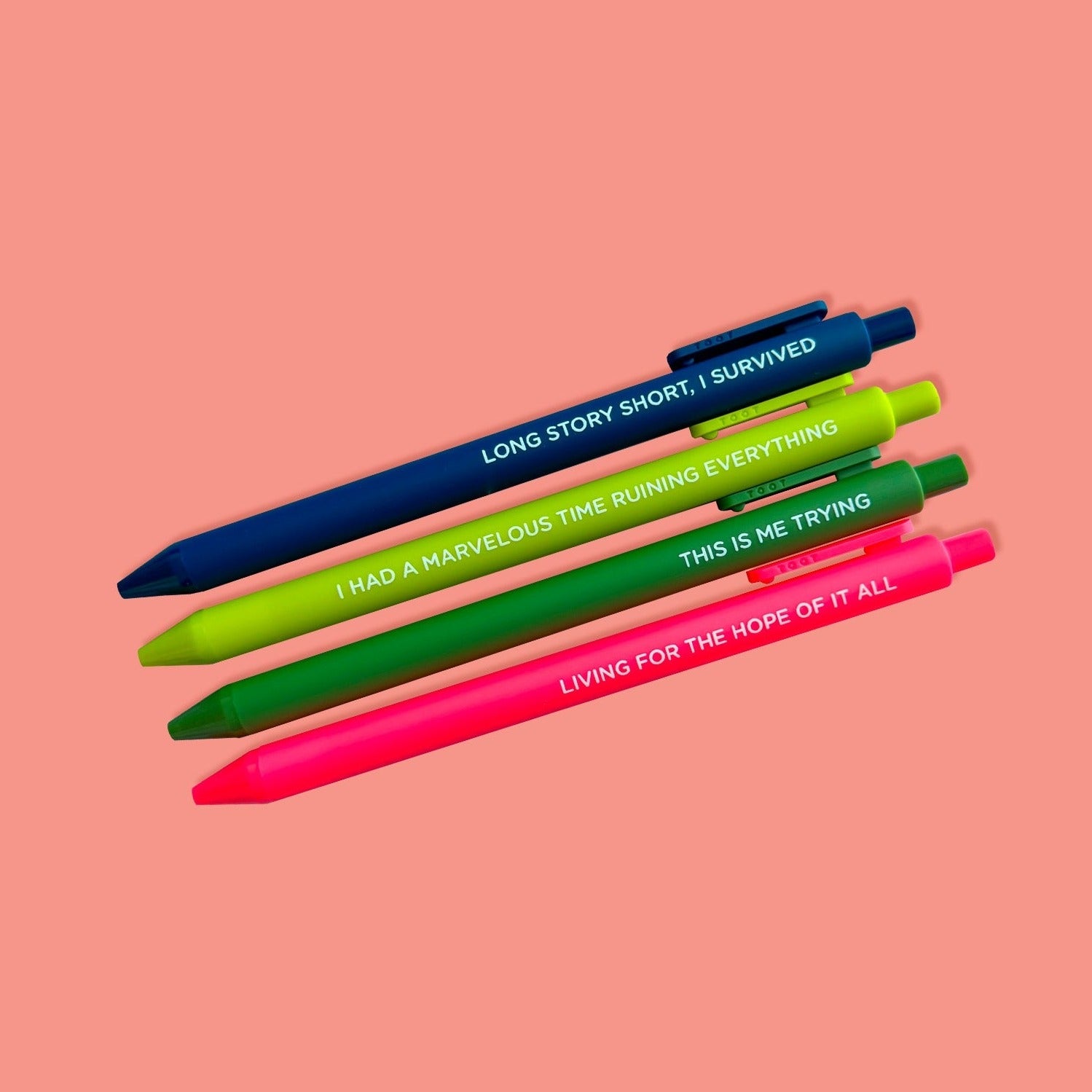 On a coral pink background sits a set of 4 pens. These Taylor Swift inspired pens are in brights colors of navy, chartreuse, green, and hot pink. They say "LONG STORY SHORT, I SURVIVED", "I HAD A MARVELOUS TIME RUINING EVERYTHING", "THIS IS ME TRYING", and "LIVING FOR THE HOPE OF IT ALL."